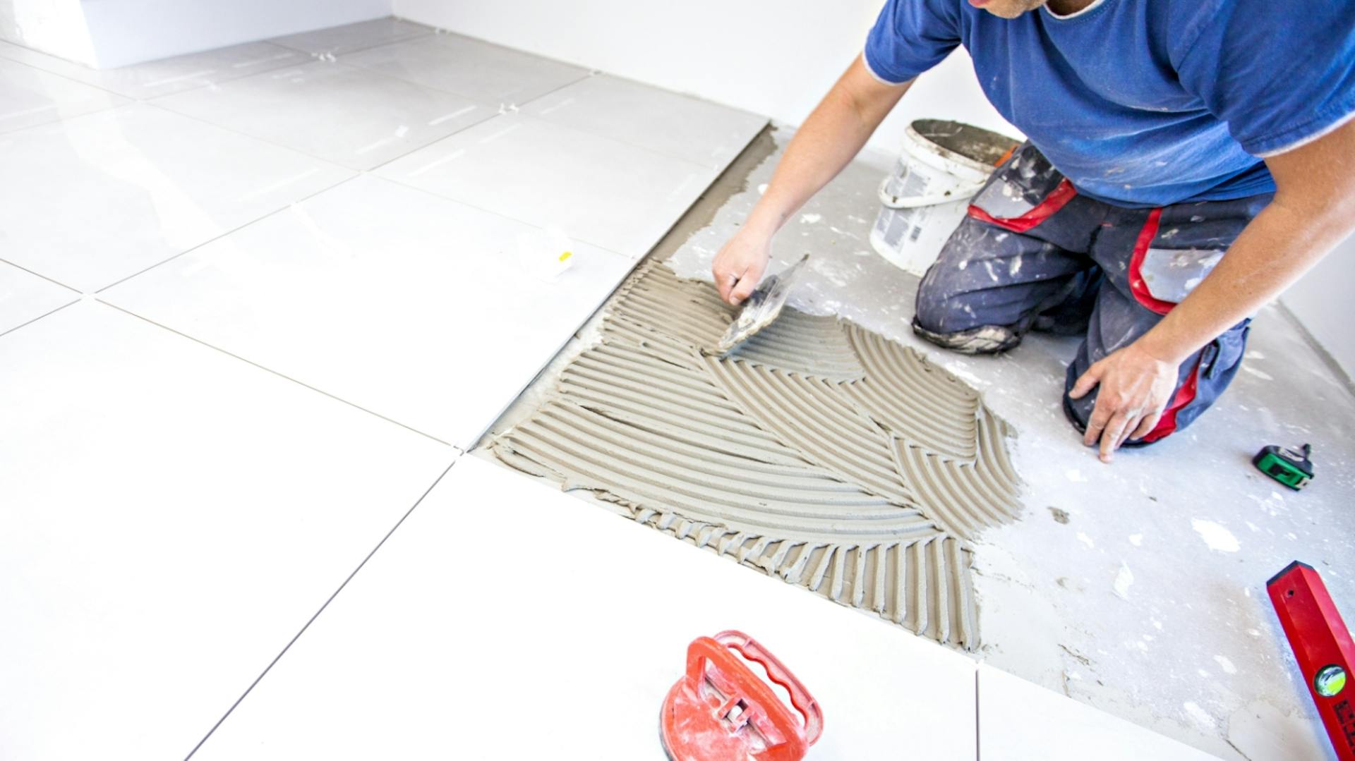 Una persona piastrella un pavimento con grandi piastrelle bianche.