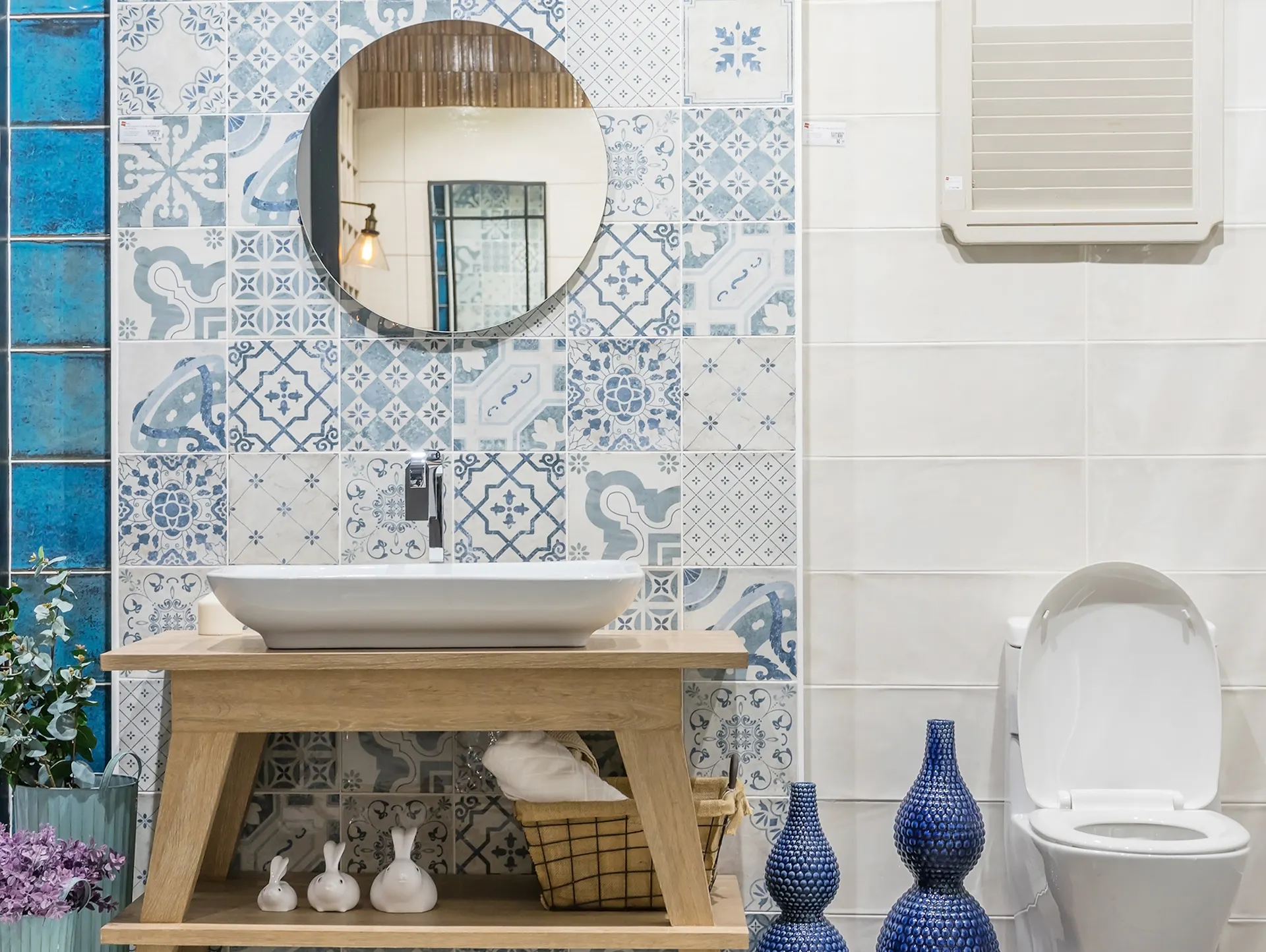 Mobile lavabo in legno con lavabo bianco. Sullo sfondo, piastrelle con motivi azzurri. Accanto, piastrelle bianche dietro al sanitario.