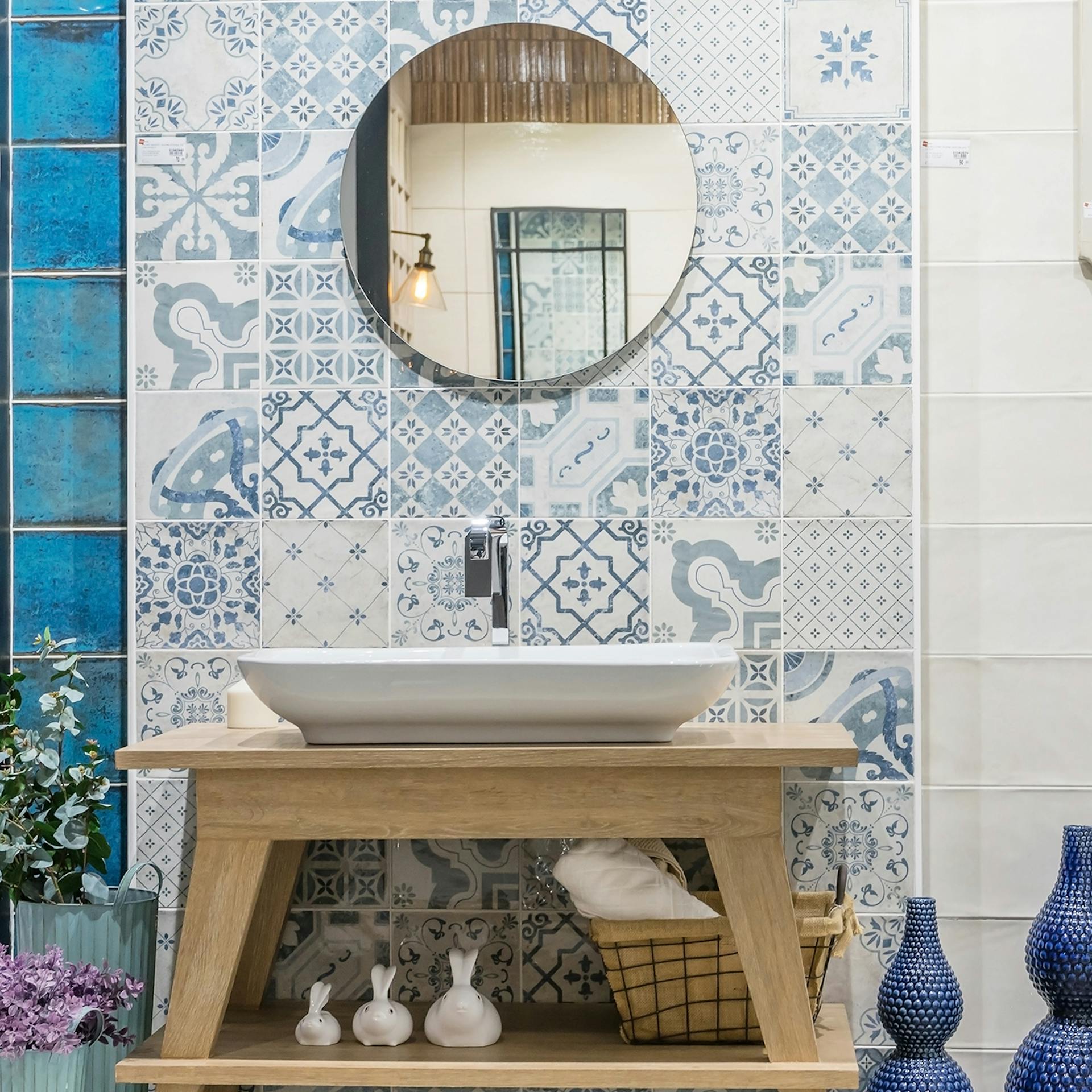 Mobile lavabo in legno con lavabo bianco. Sullo sfondo, piastrelle con motivi azzurri. Accanto, piastrelle bianche dietro al sanitario.