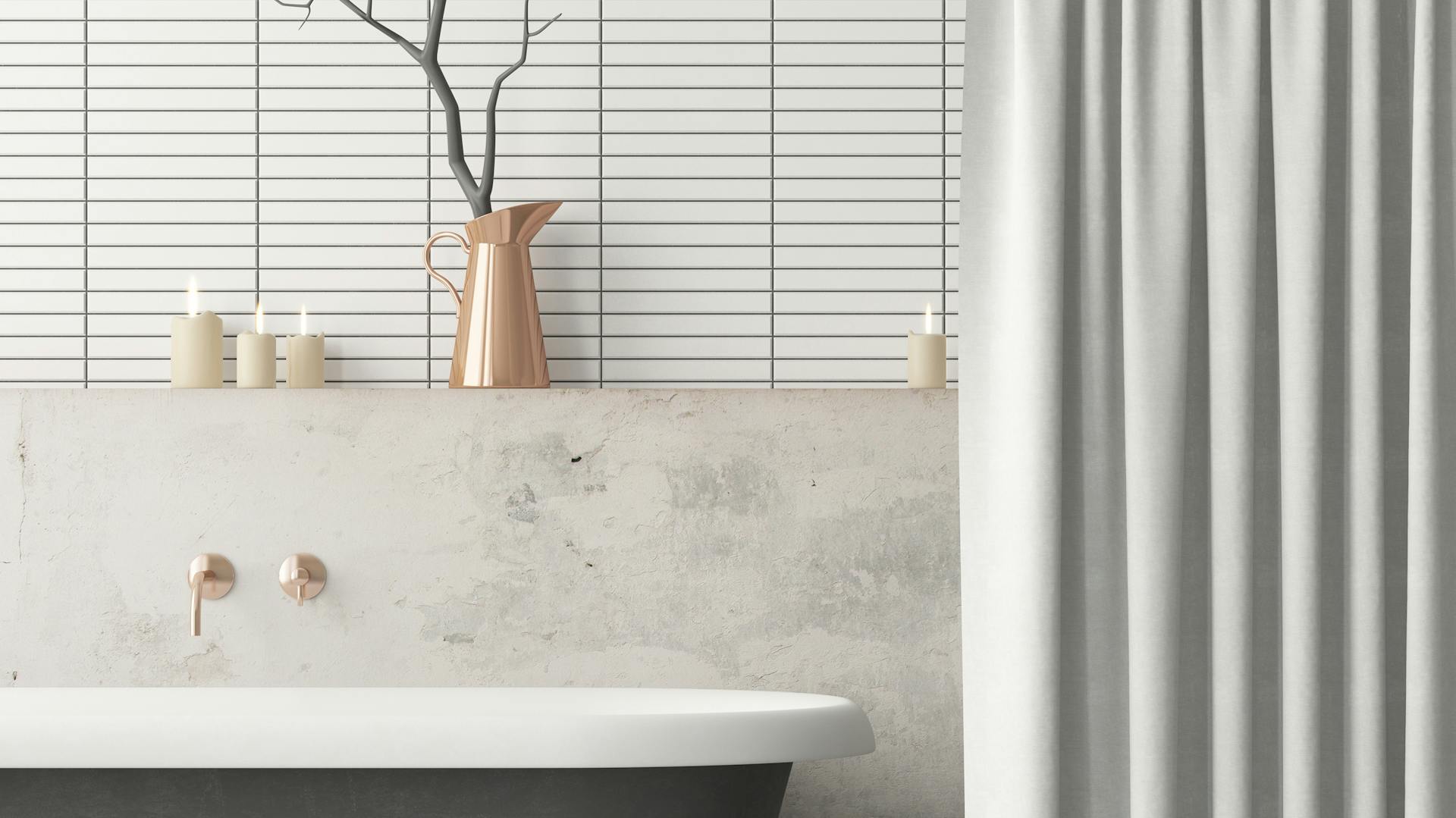 Sivá vaňa s mramorovými obkladačkami na stene a medenými doplnkami.