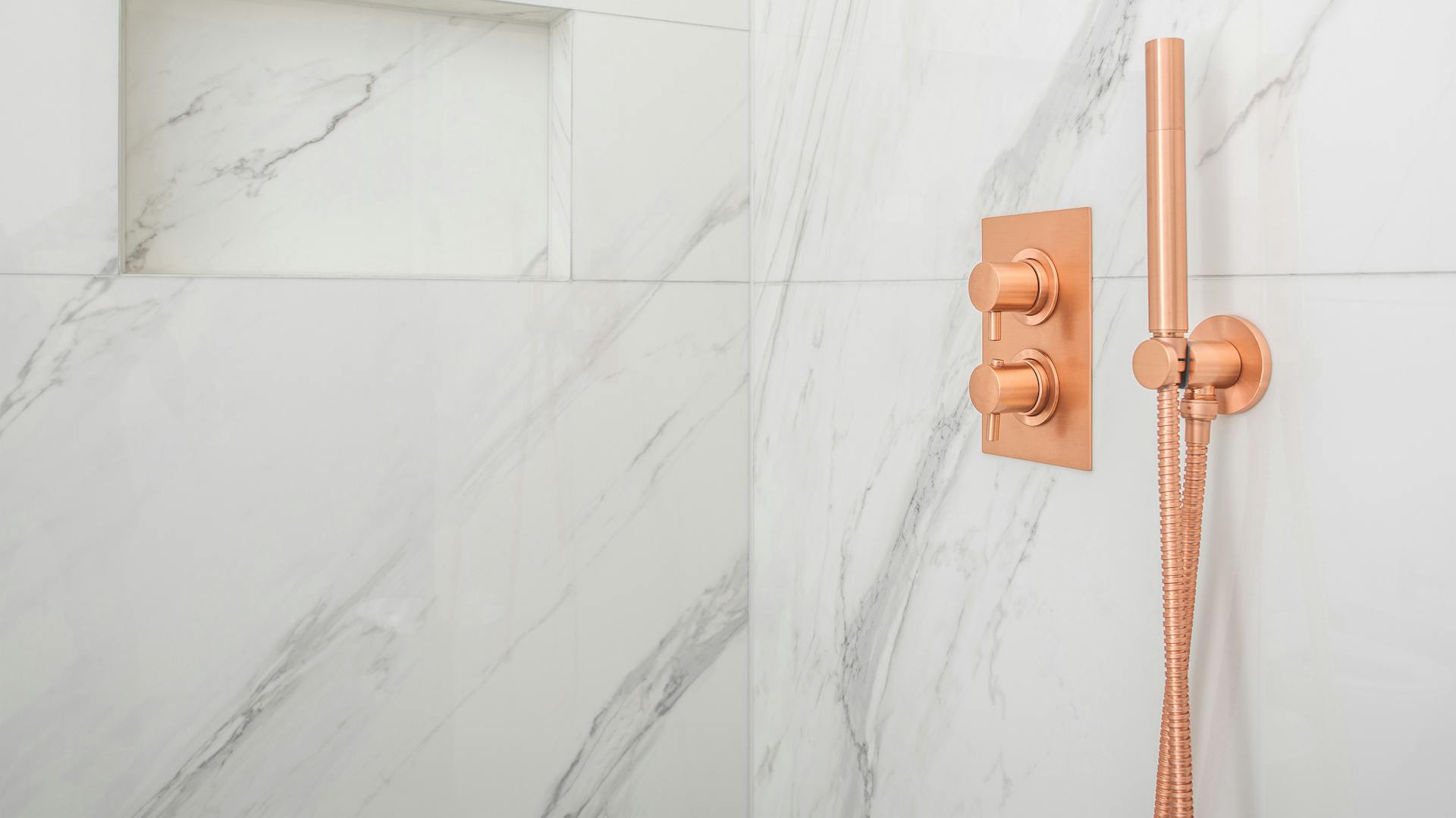 Mramorové obkladačky v bielej farbe a medená sprchová tyč.