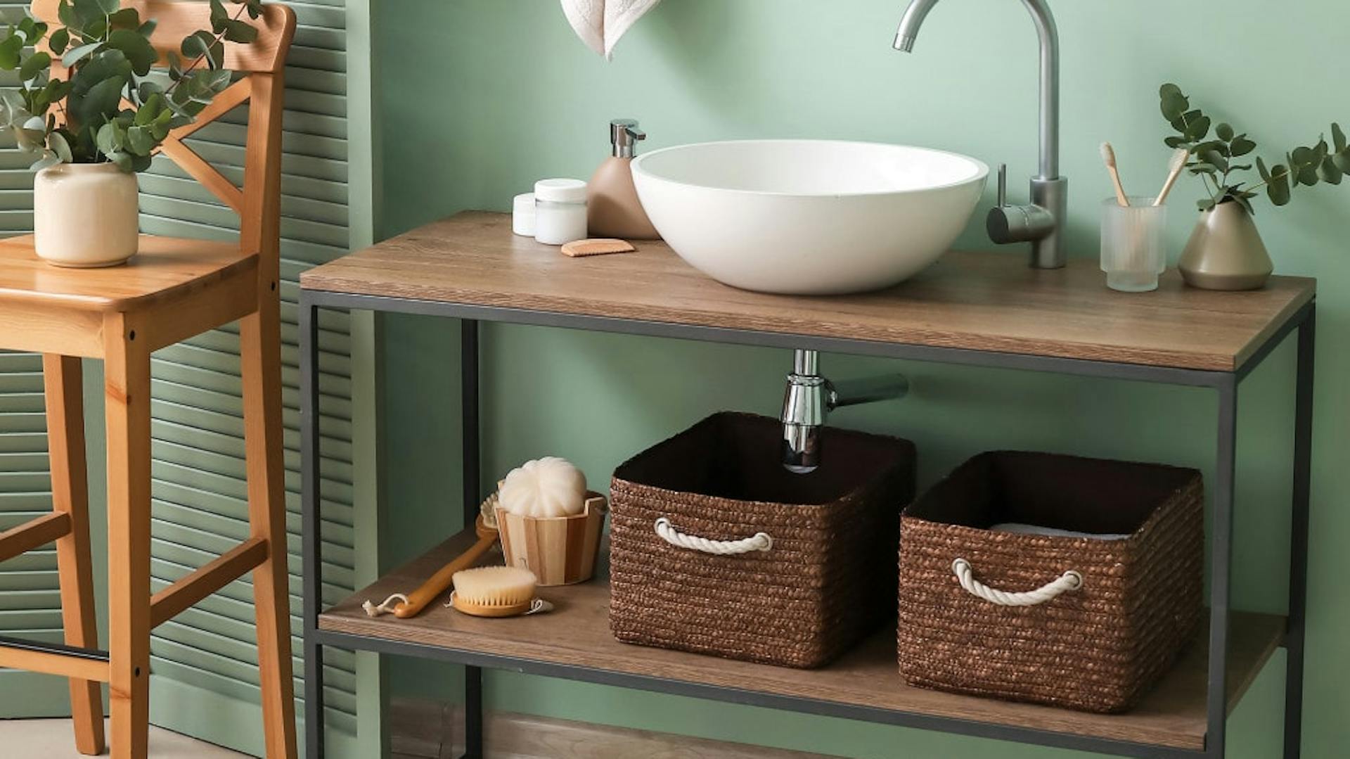 Holzwaschtisch mit Eisengestell und weißem runden Waschbecken vor türkisfarbener Wand.