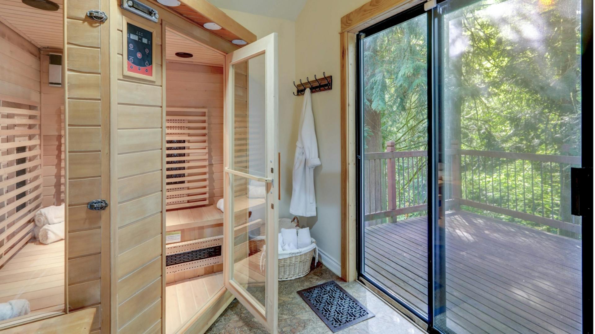 Una sauna di legno in una stanza luminosa con porta sulla terrazza e vista sul verde.