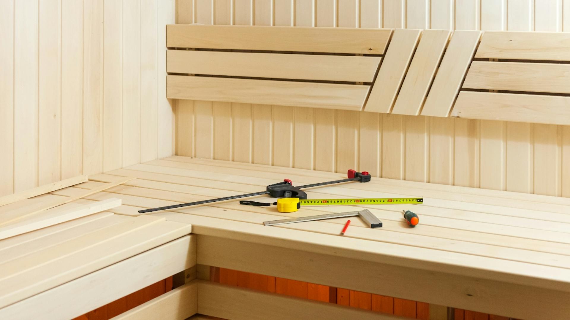 Saunabank aus Holz, darauf liegen verschiedene Werkzeuge für den Saunabau wie Metermaß und Schraubenzieher.