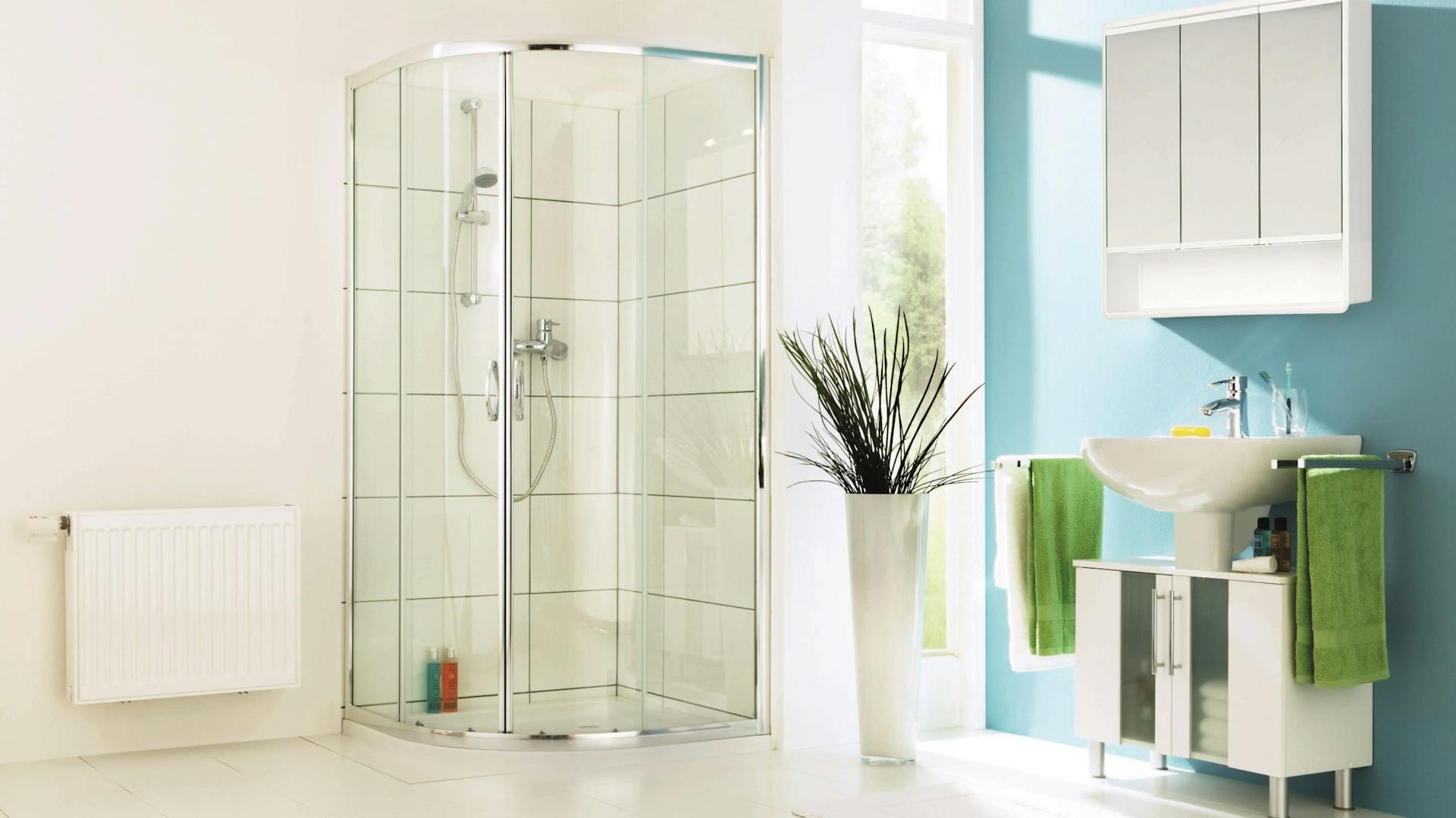 Dusche mit Viertelkreis-Duschwanne für Schlauchbad an weißer Wand neben Heizung Fenster Stehpflanze Waschbecken und Spiegelschrank