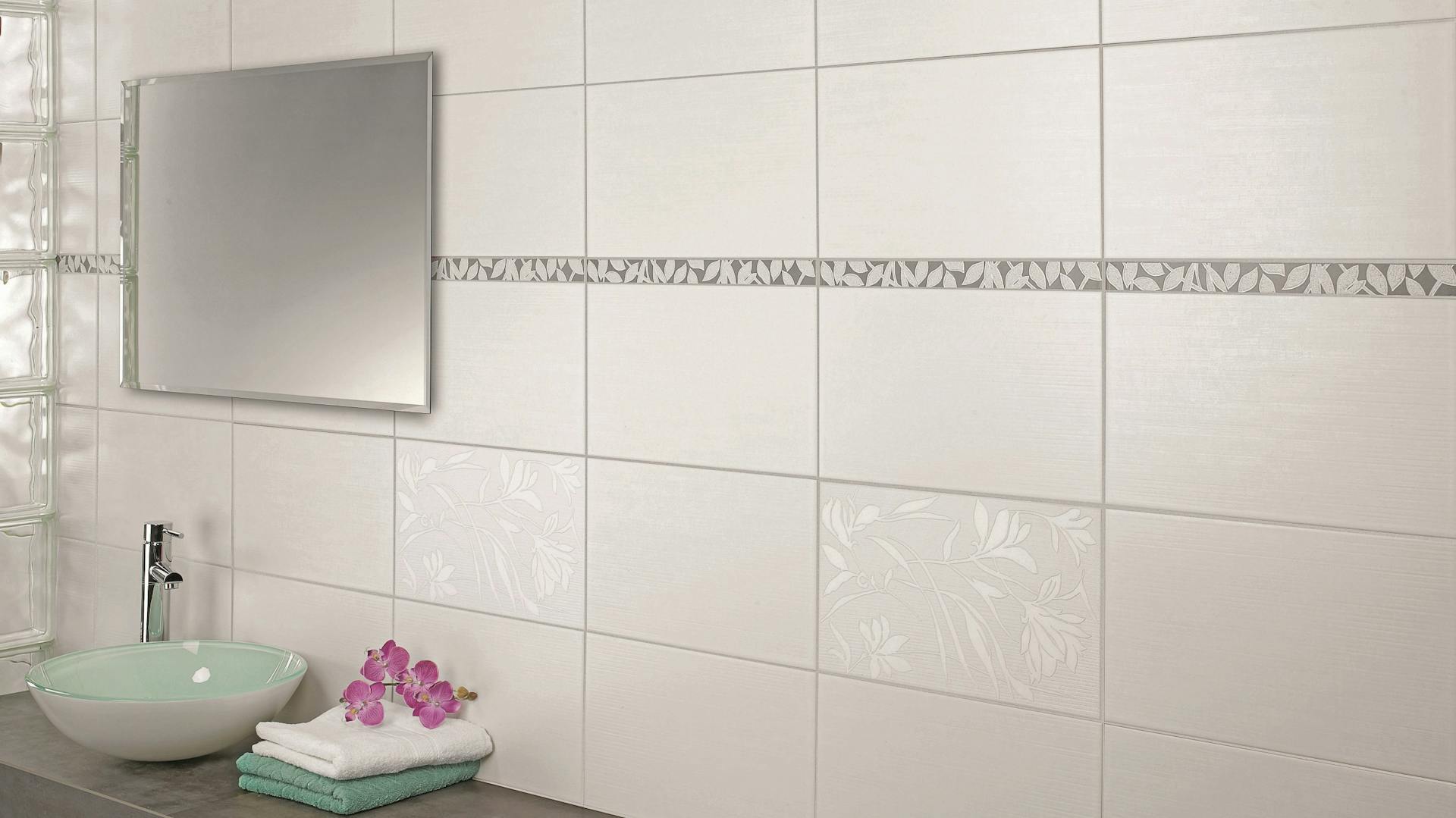 Badwand mit großen Fliesen, Spiegel, Waschbecken und Handtüchern auf Ablage neben Raumtrenner aus Glasbausteinen