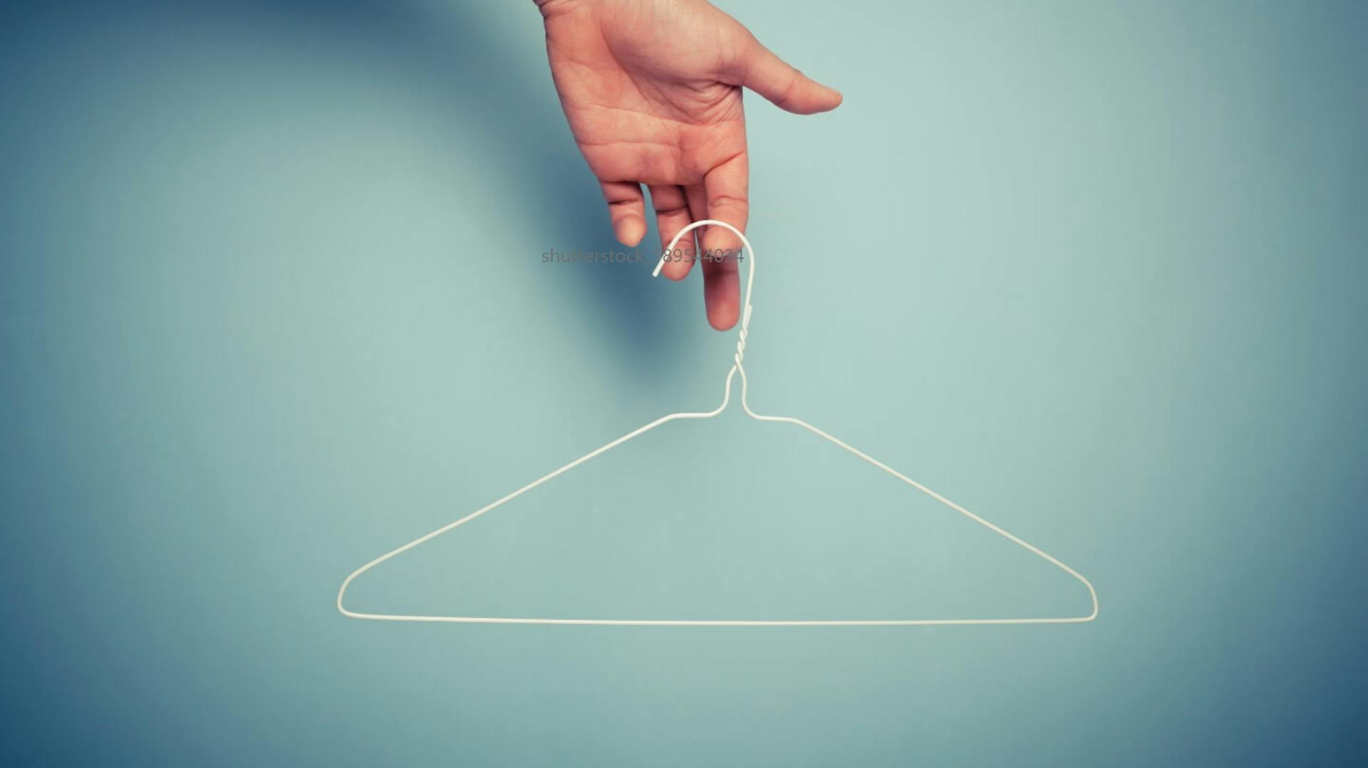 Egy kéz egy fehér drótvállfát tart egy kék fal előtt.