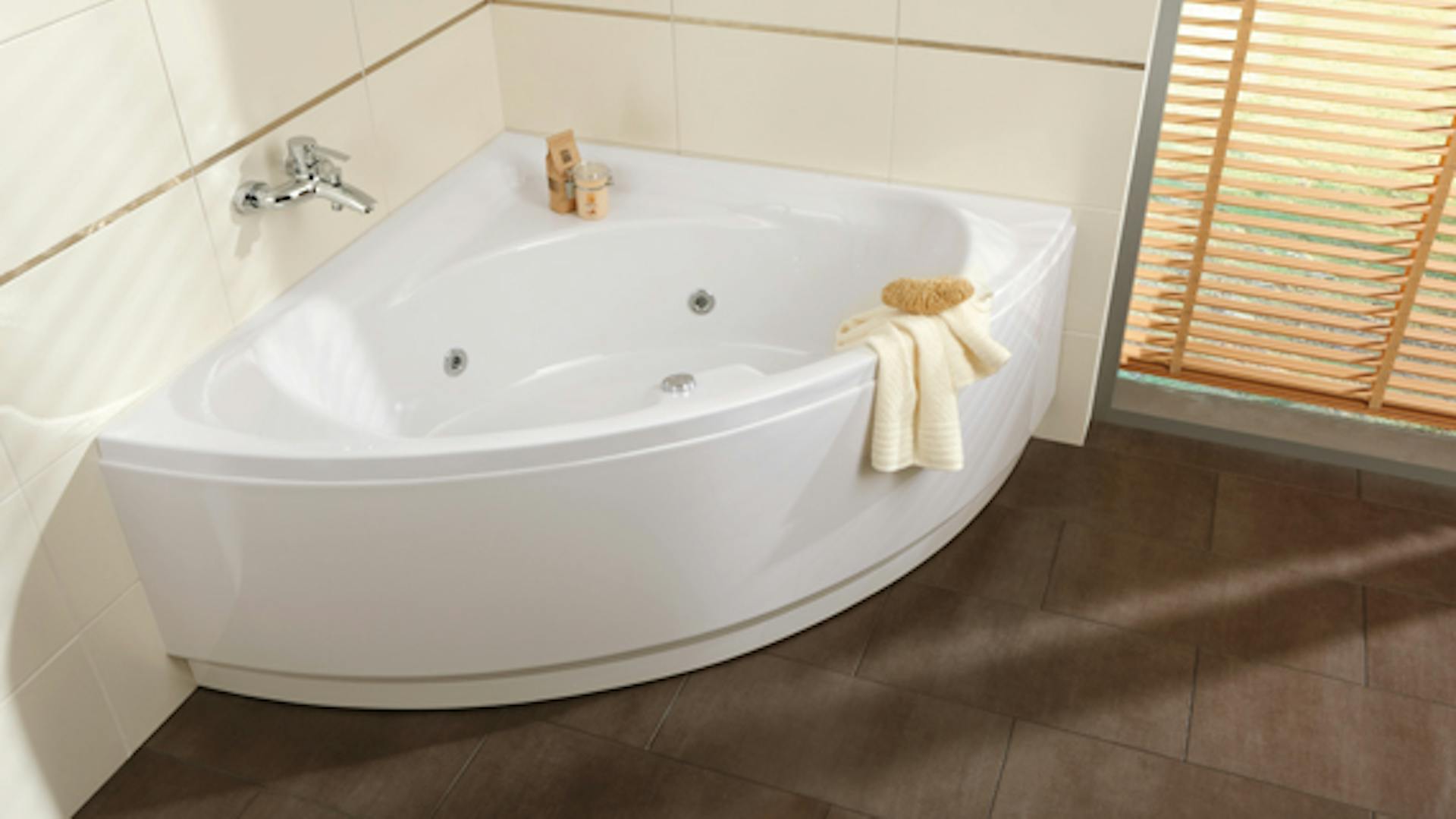 Eckbadewanne vor weißer Badezimmerwand mit Armatur und Handtuch.