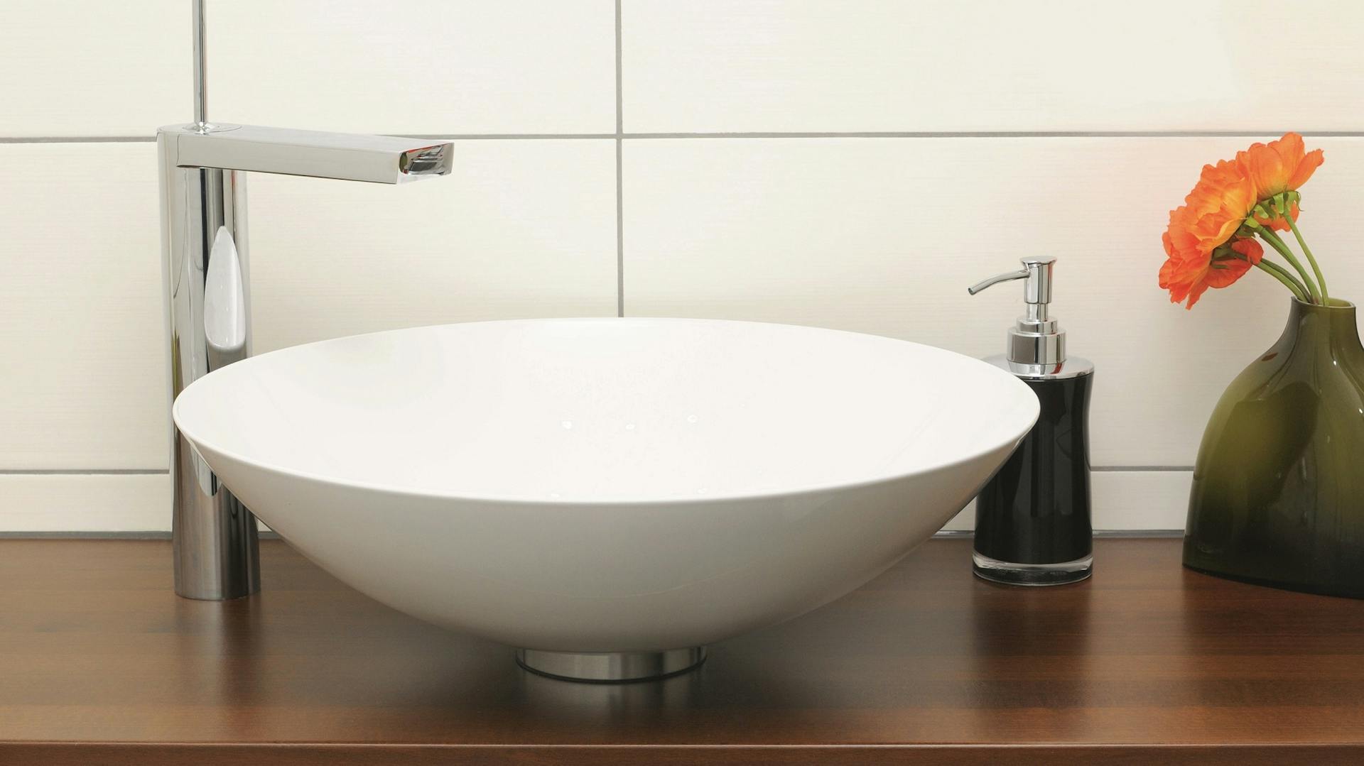 Weißes Aufsatzwaschbecken auf Holzplatte mit Wasserhahn und Seifenspender.