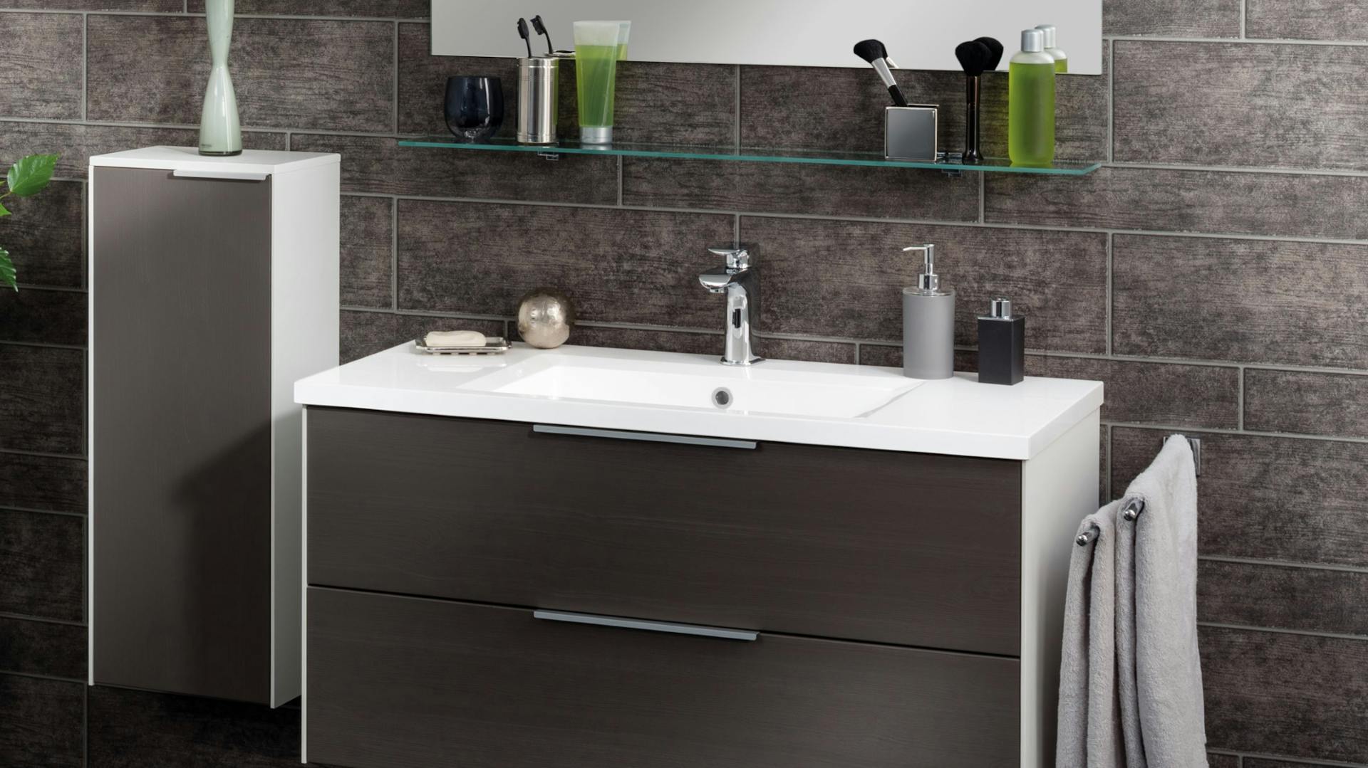 Weißes Waschbecken aus Mineralguss auf Unterschrank mit dunklen Schubladen vor anthazit gefliester Wand.