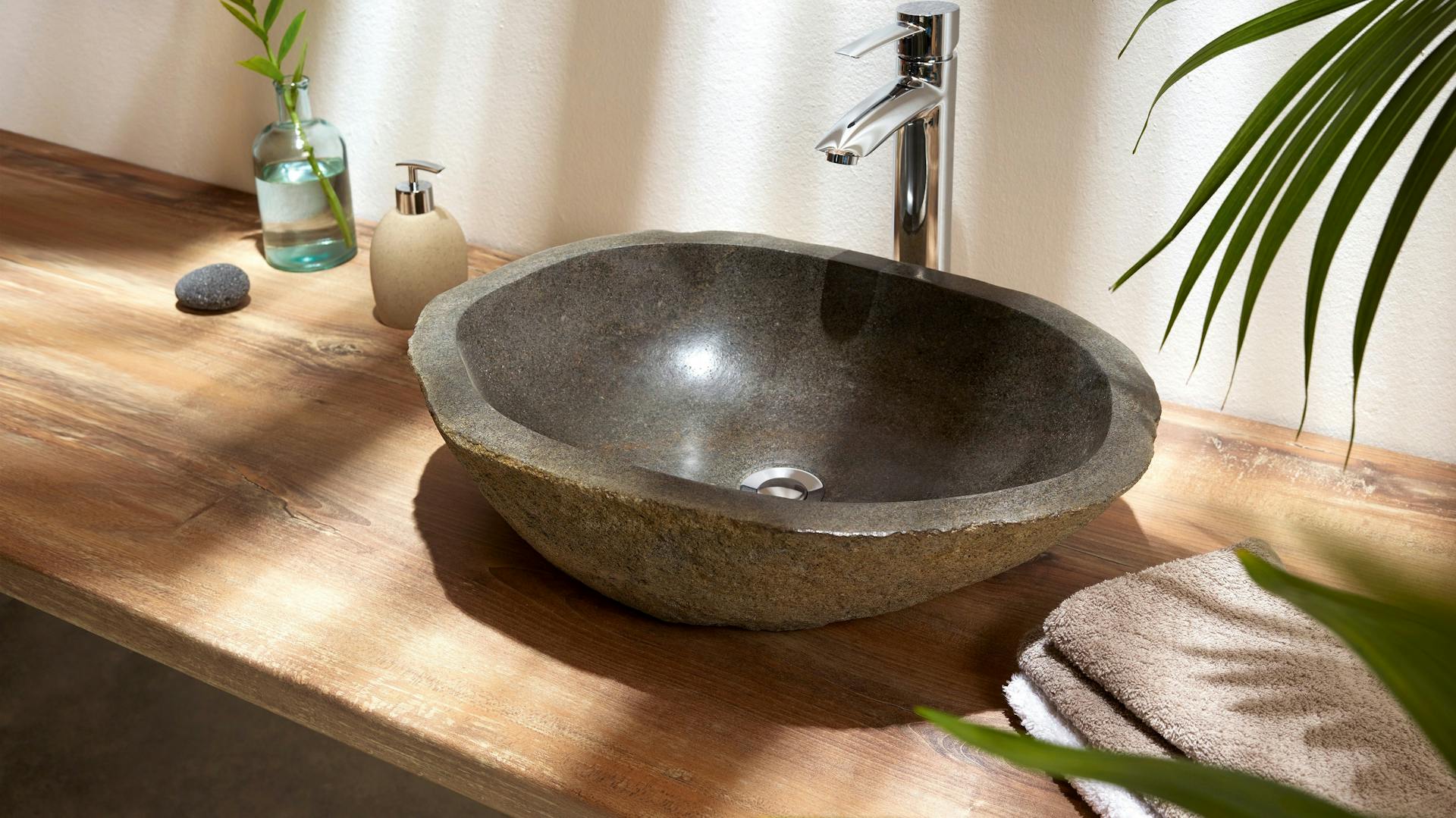 Aufsatzwaschbecken in Naturoptik auf Holzplatte mit Pflanzen und Handtüchern.