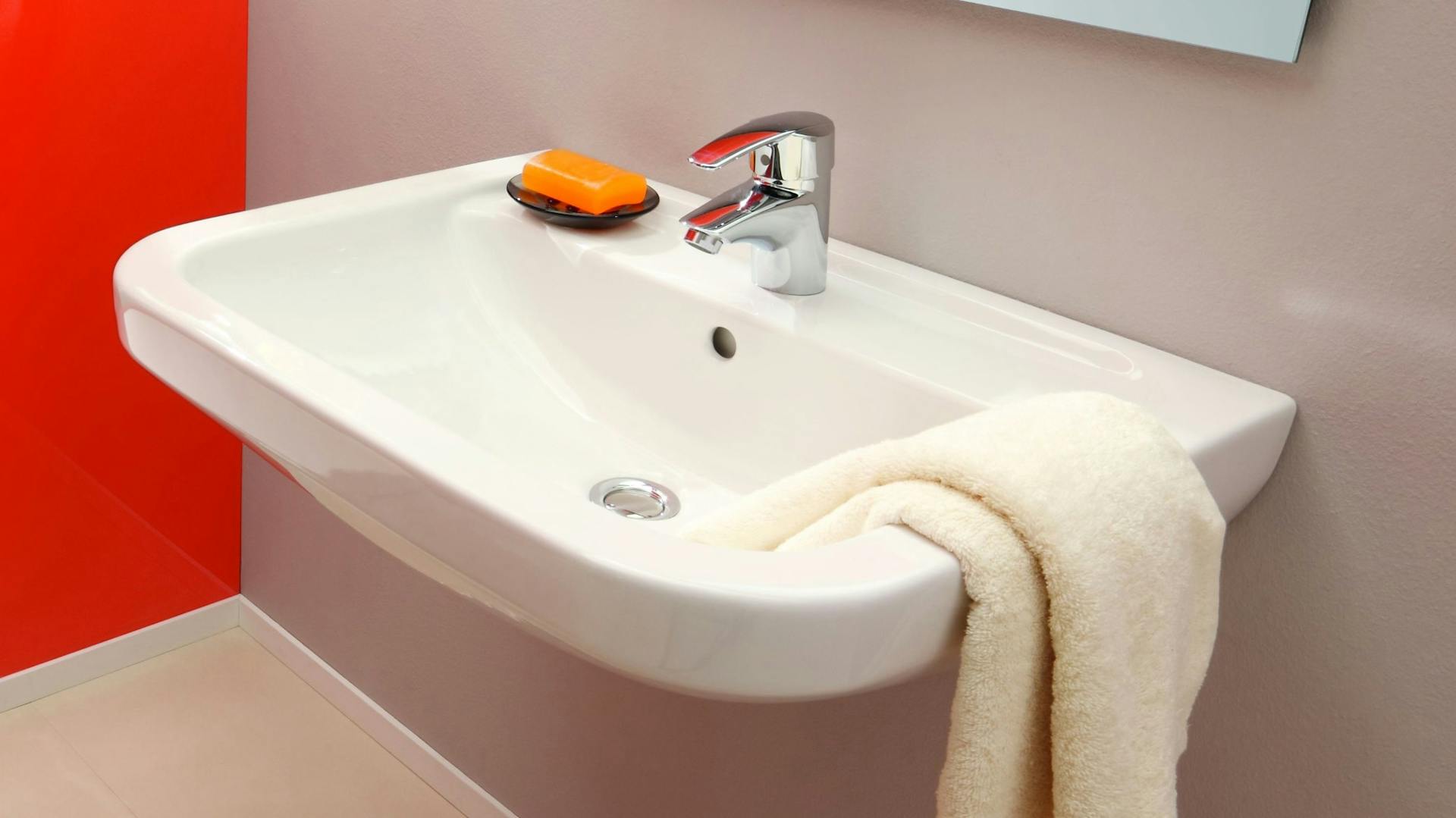 Klassisches weißes Waschbecken aus Keramik mit silberner Armatur und beigem Handtuch über dem Beckenrand.