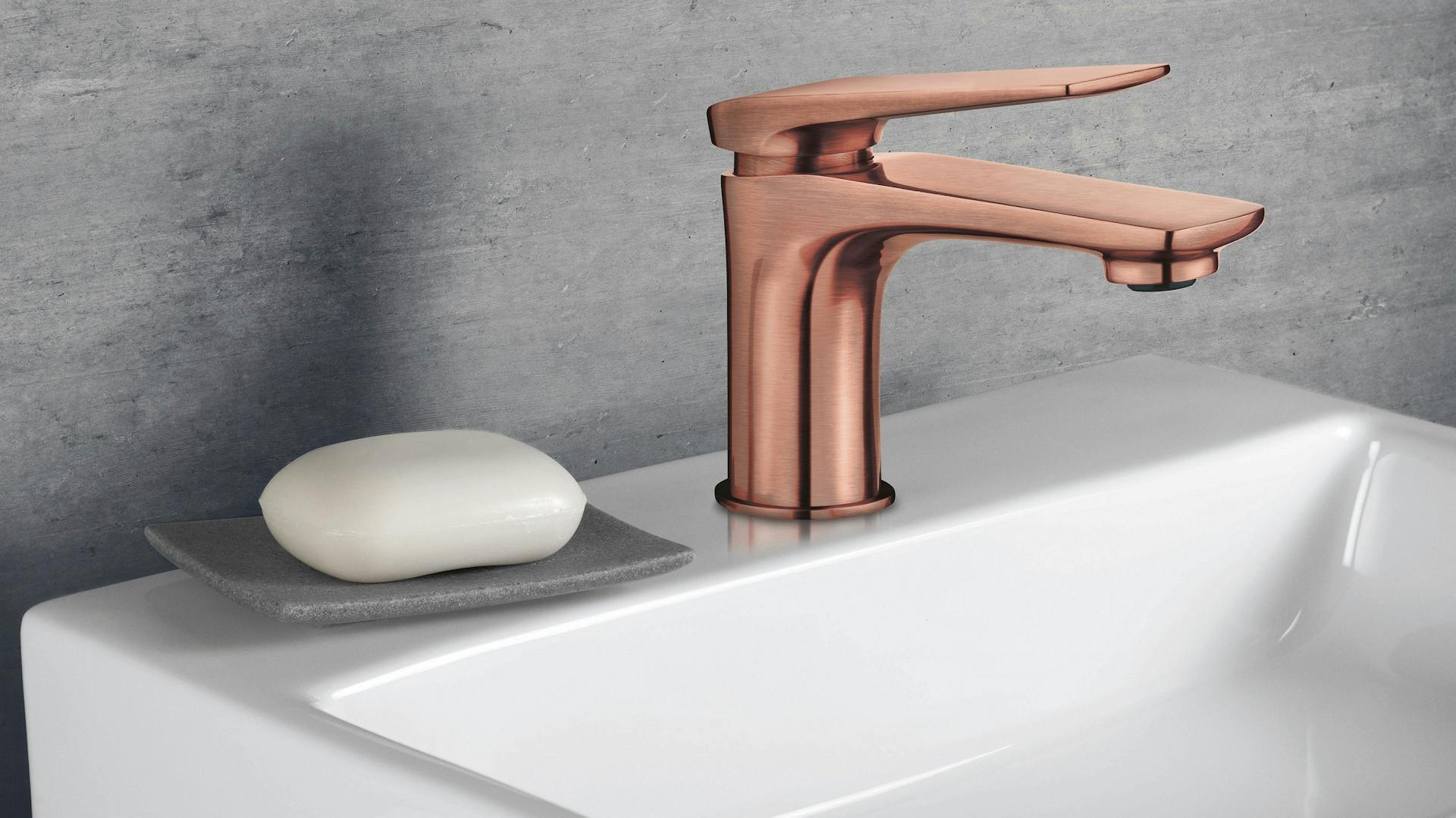 Waschbeckenarmatur aus Kupfer auf weißem Waschbecken vor grauer Wand.