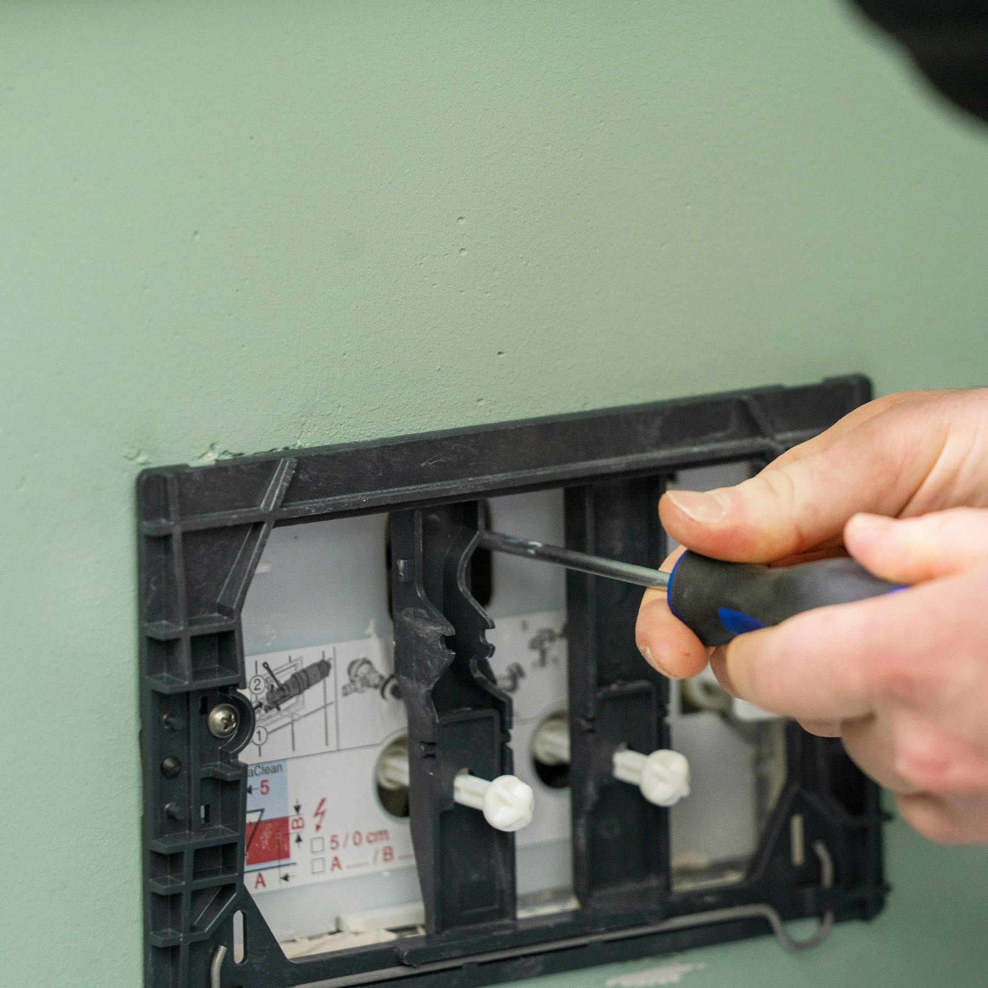 Heimwerker dreht Eckventil mit einem Schraubenzieher zu.