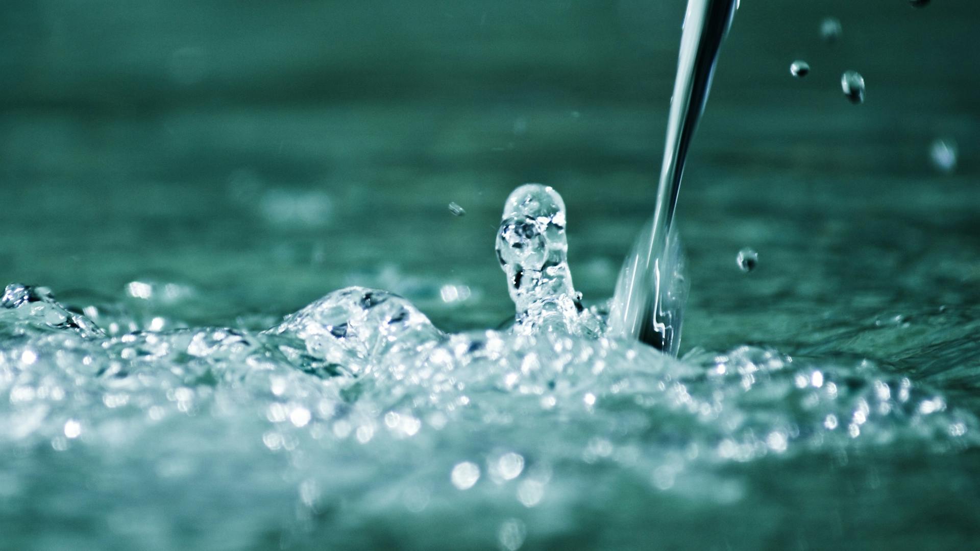 Wasserstrahl trifft perlend auf Wasseroberfläche auf.