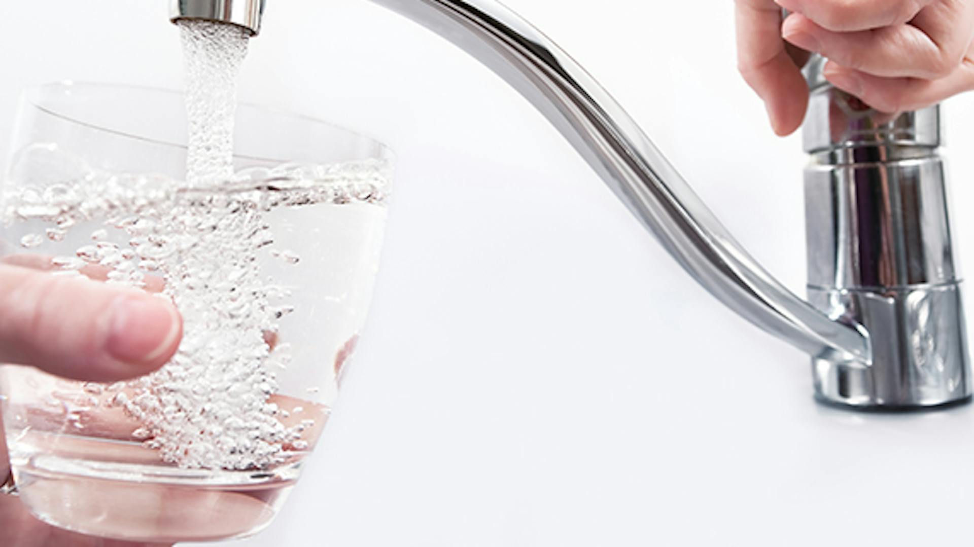 Jemand lässt Wasser aus einem Wasserhahn in ein Glas laufen.