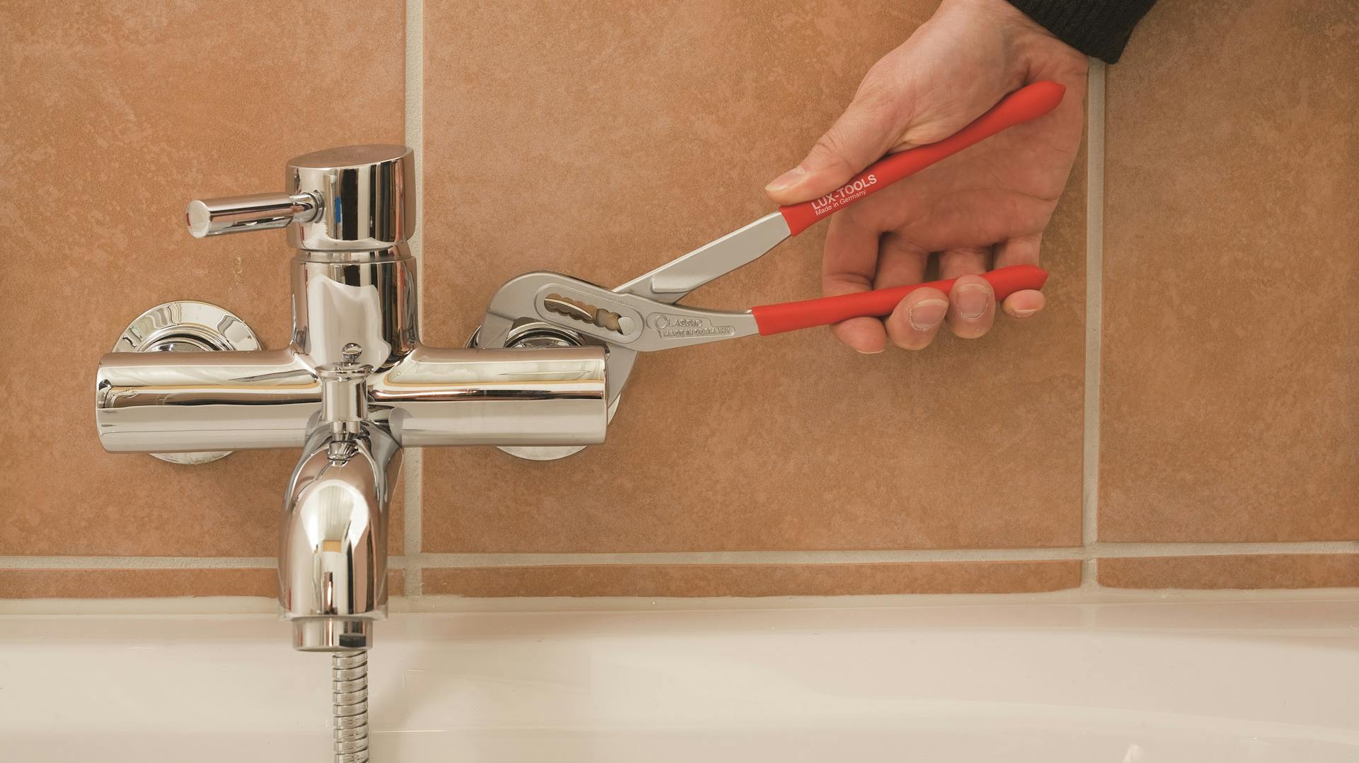 Heimwerker installiert Armatur an der Badewanne.