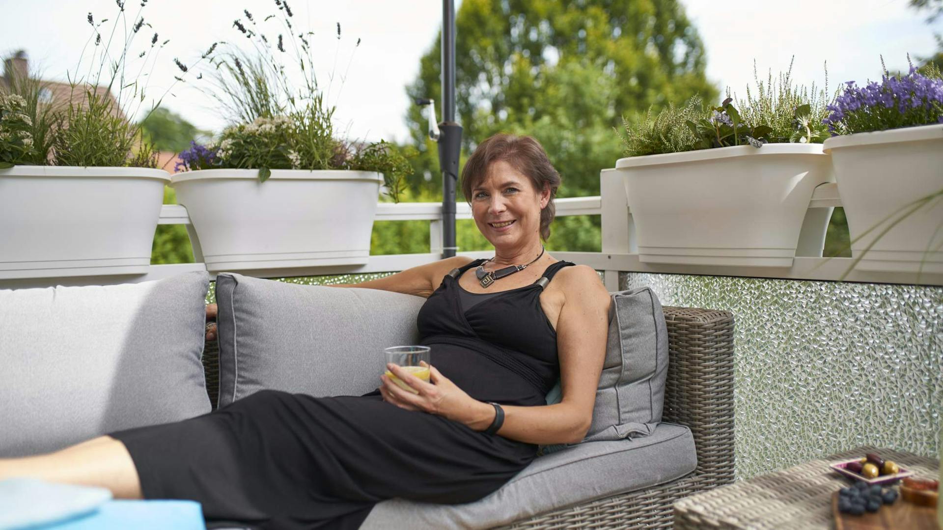 Frau mit Getränk sitzt auch Gartenlounge