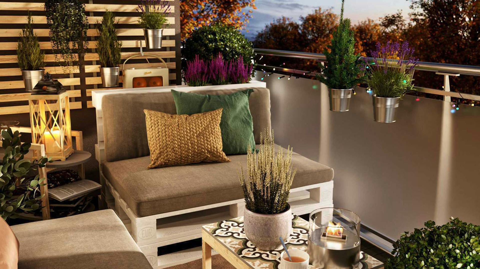 Palettencouch Bankig steht auf einem Balkon der mit Lichterketten geschmückt ist und der eine Sprossenwand besitzt an den Pflanzen aufgehängt sind.