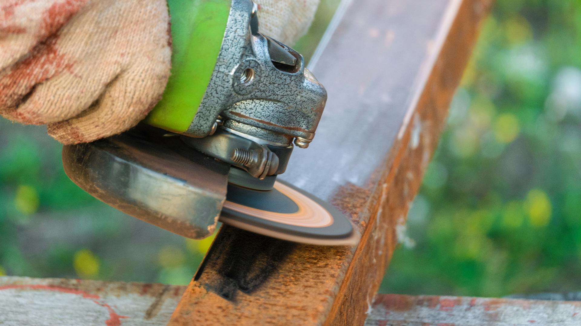Heimwerker schleift Rost vom Balkongeländer mit Schleifmaschine und Handschuhen ab.