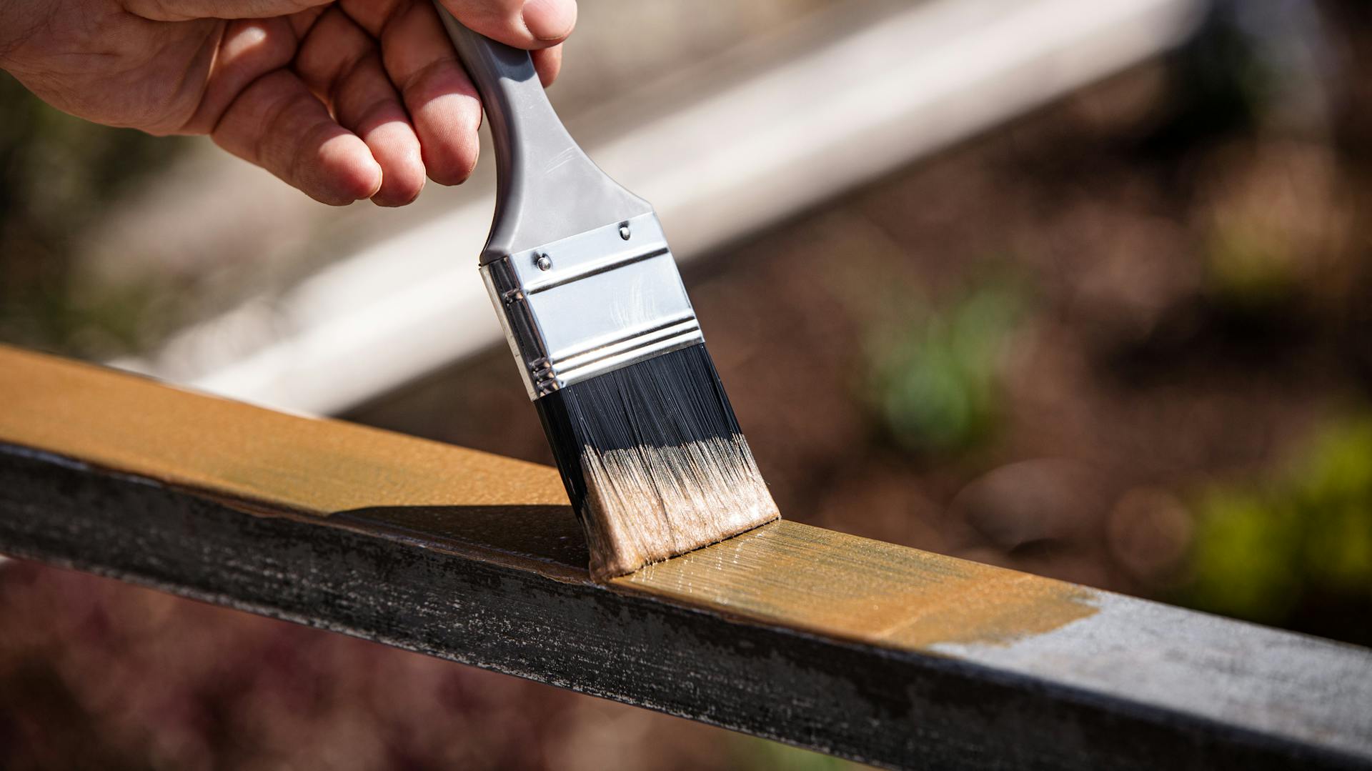 Person streicht Geländer mit Pinsel und Farbe.
