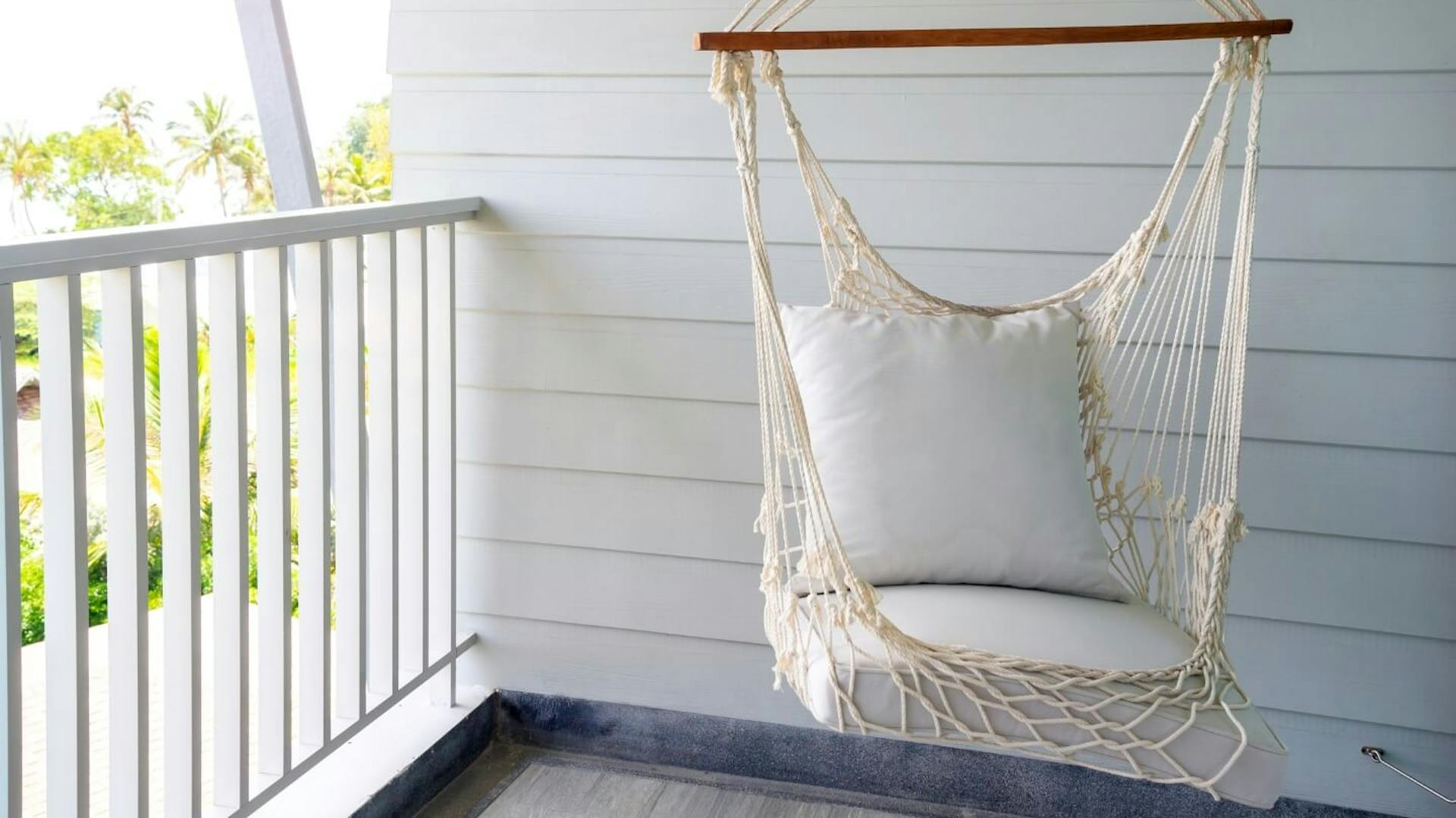 Függőszék fehér párnákkal egy fehér korlátos erkélyen