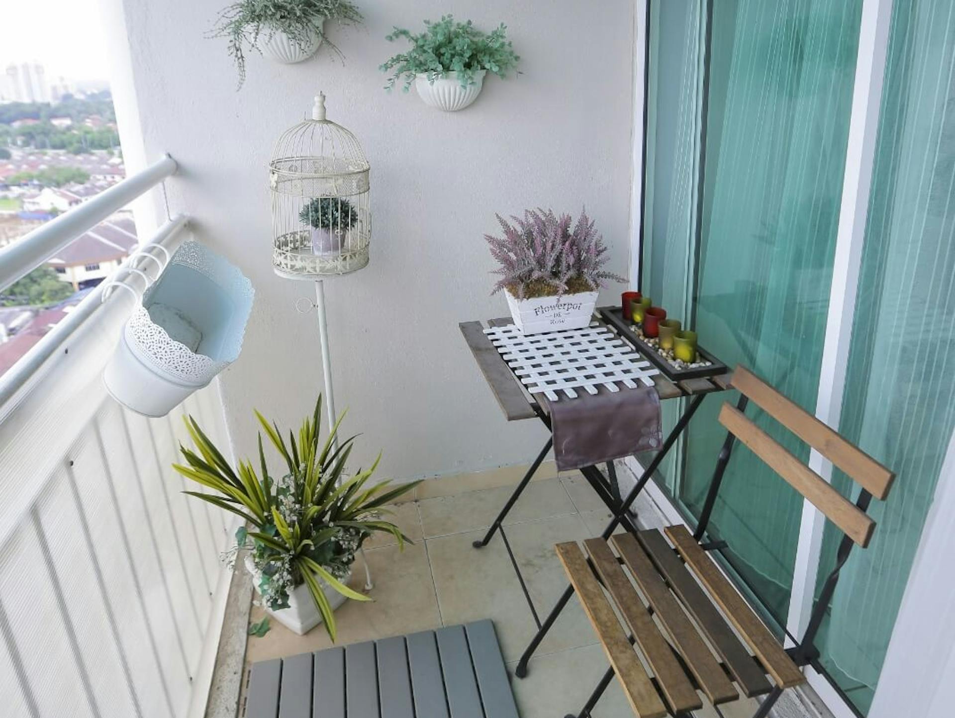 Keskeny erkély összecsukható székekkel és asztallal, valamint növényekkel a falon.