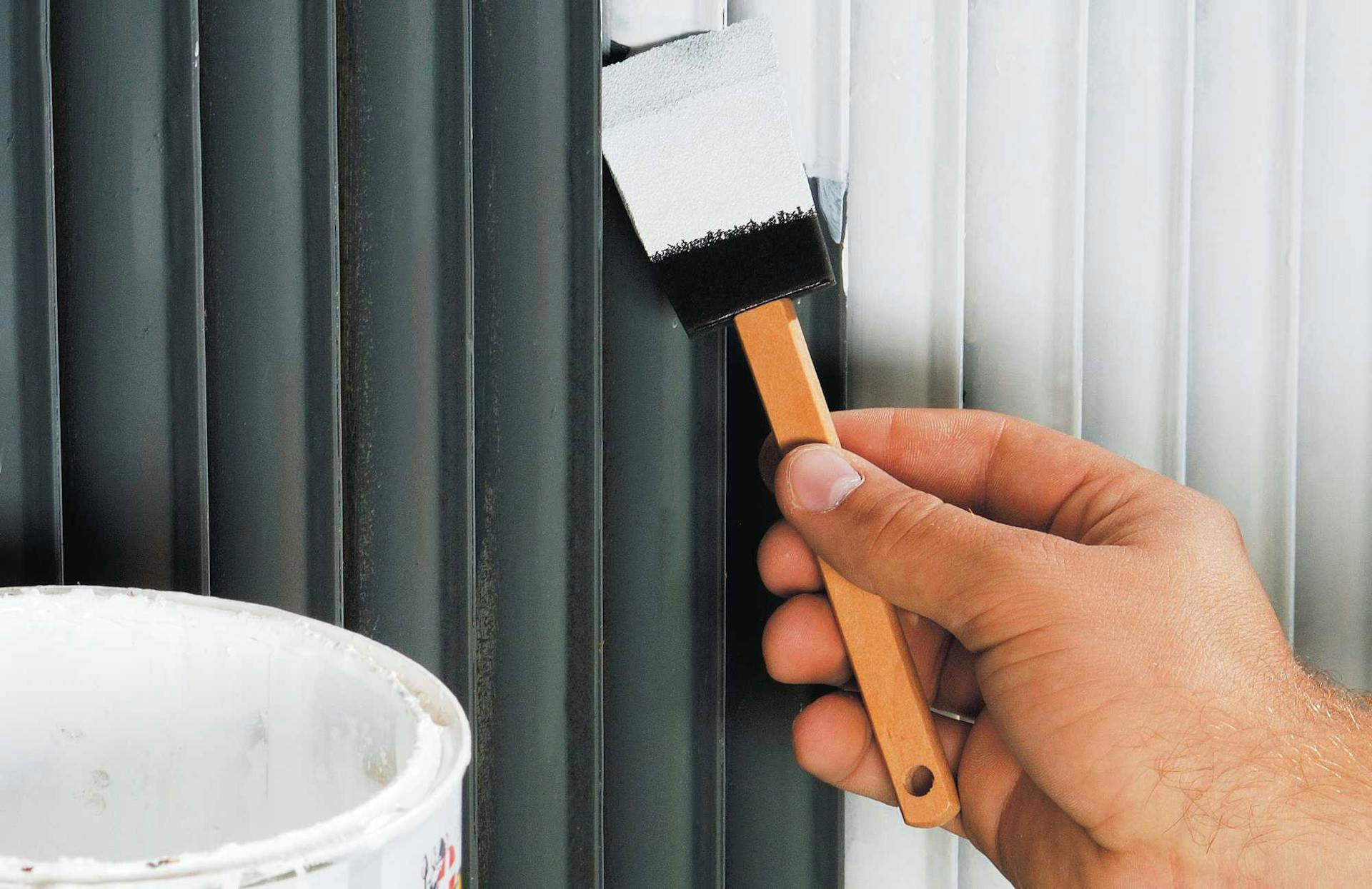 Un amante del fai da te dipinge di bianco un radiatore nero con un pennello.