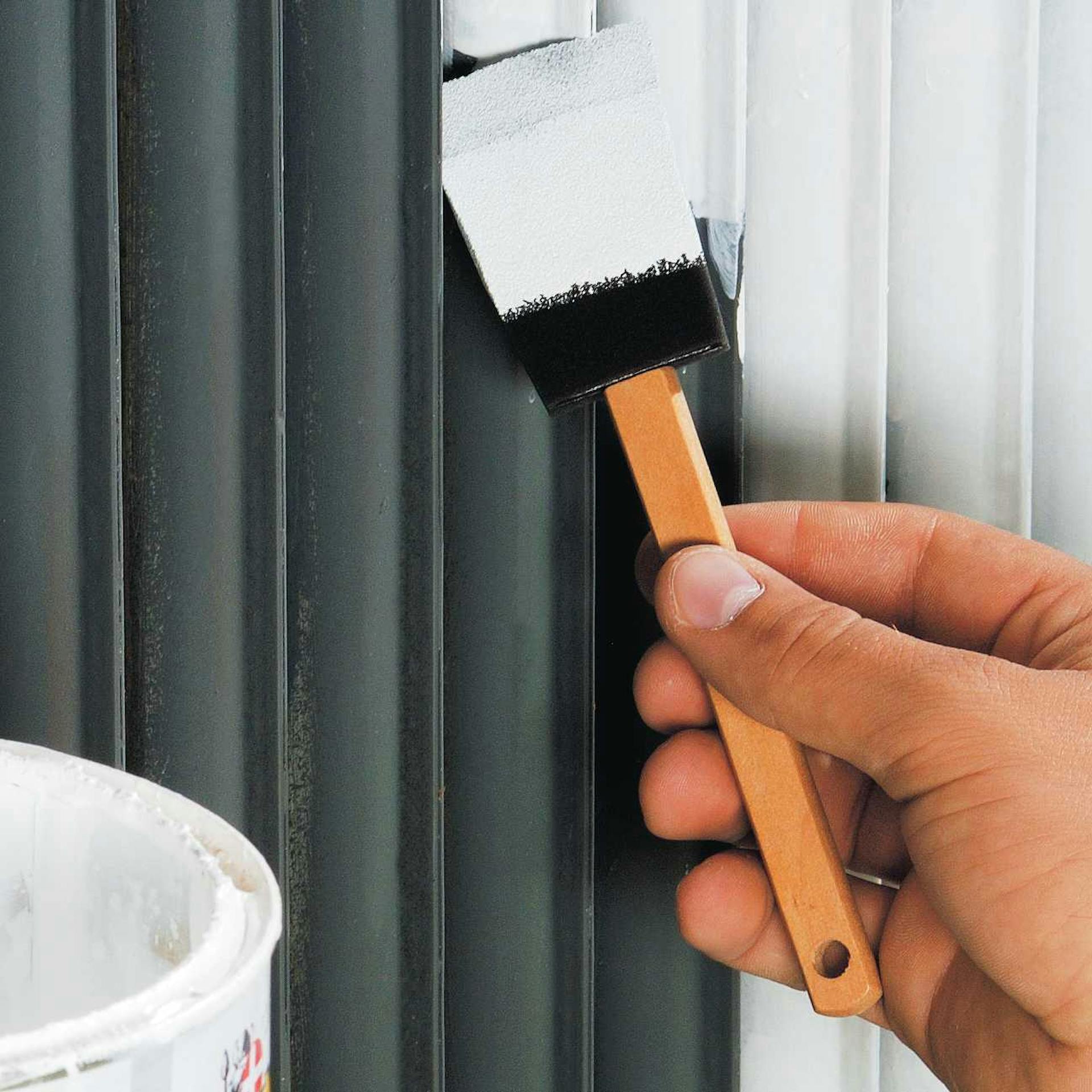 Heimwerker streicht schwarzen Heizkörper mit Pinsel in weißer Farbe.