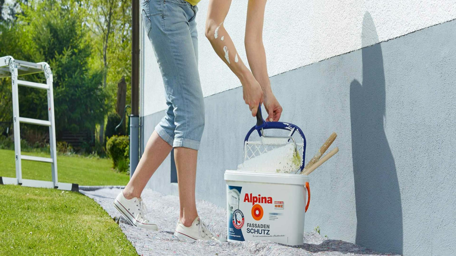 Heimwerkerin streicht Untergrund im Außenbereich mit Fassadenfarbe.