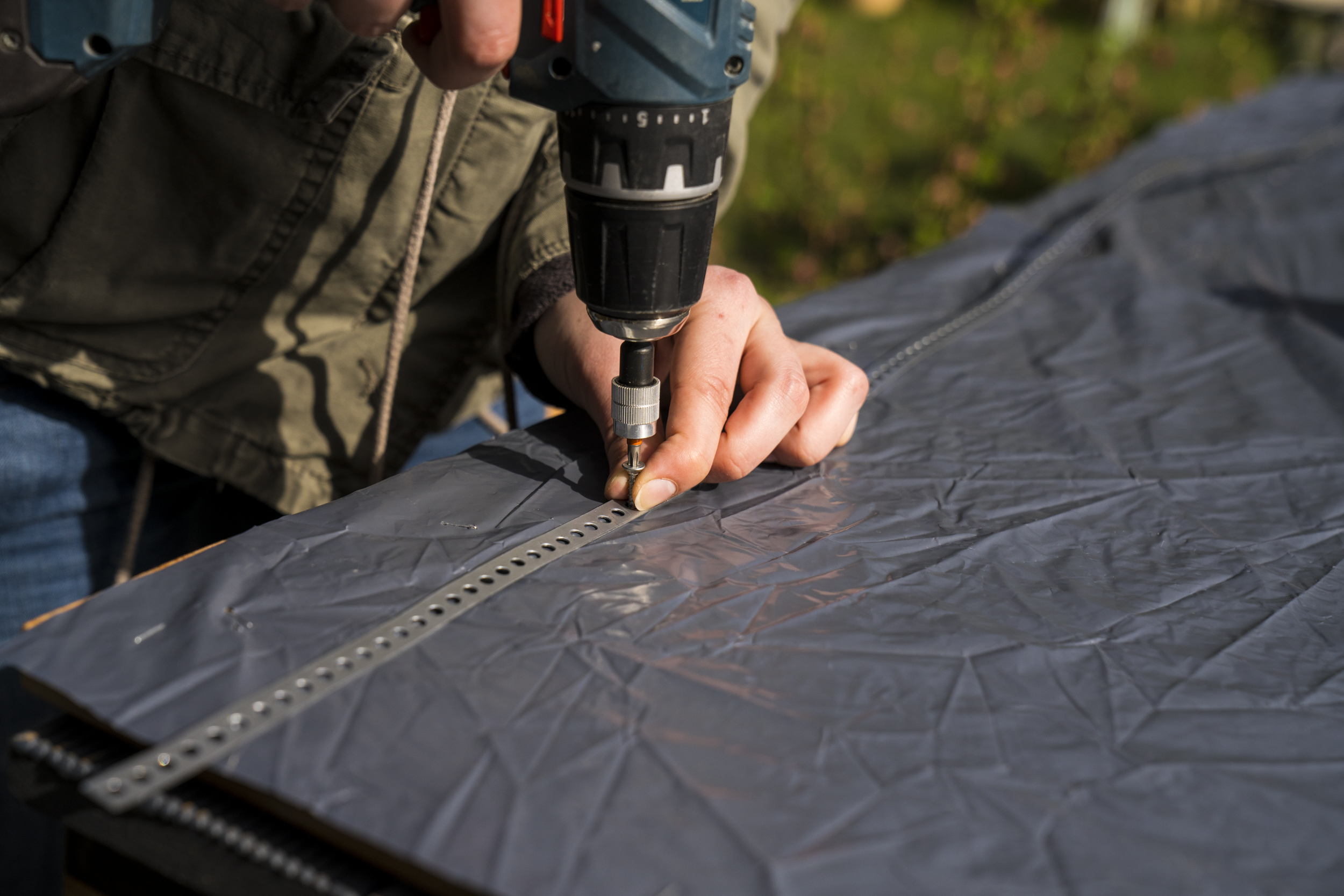 Kutil připevní děrovanou pásku na fólií vyloženou vnitřní stranu podlahových desek pomocí akumulátorového šroubováku a spojí je dohromady.