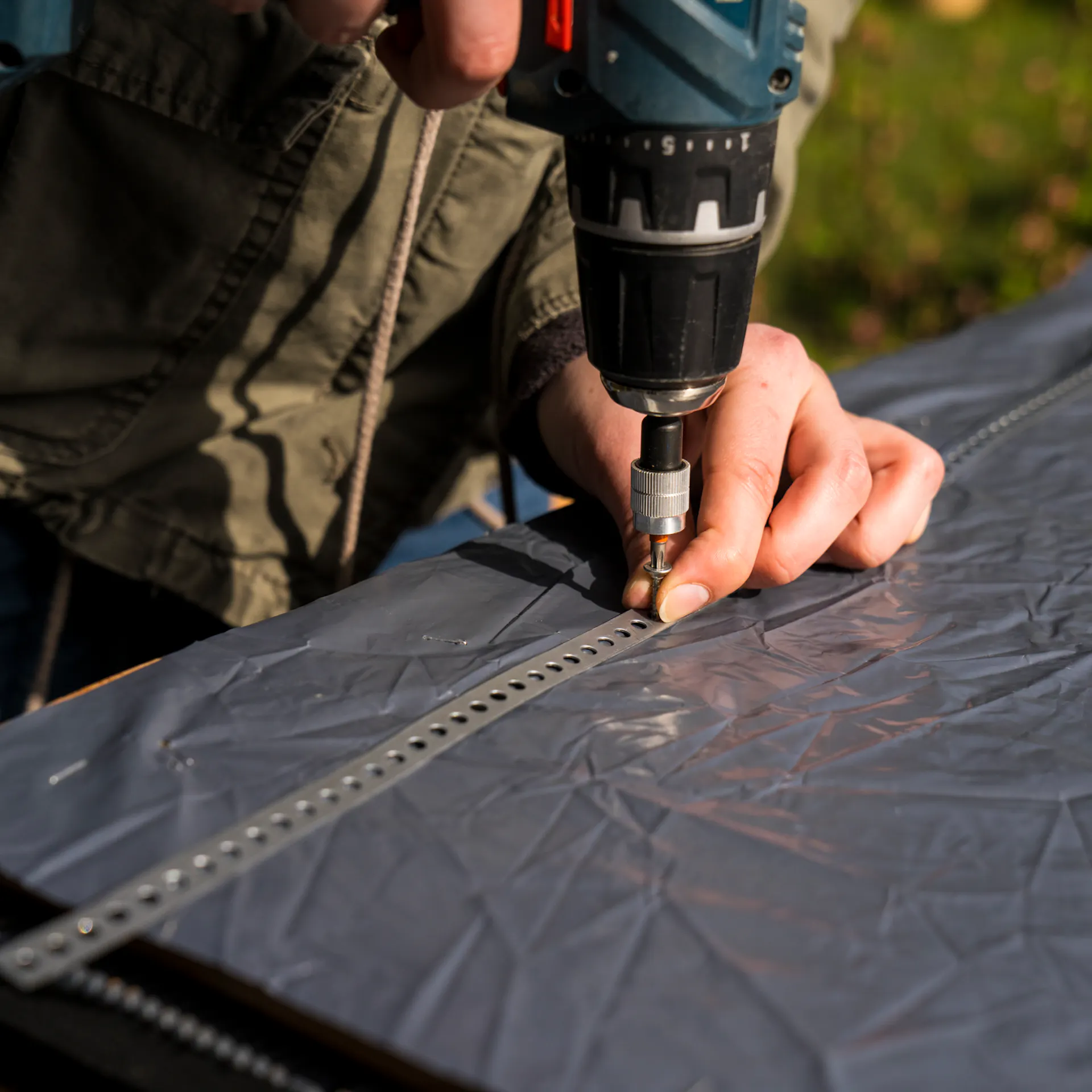 Kutil připevní děrovanou pásku na fólií vyloženou vnitřní stranu podlahových desek pomocí akumulátorového šroubováku a spojí je dohromady.