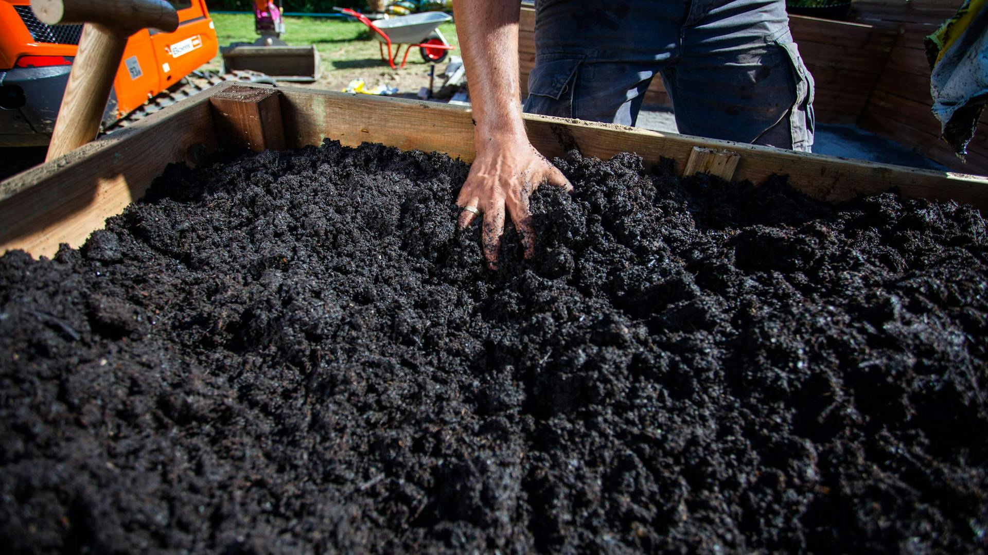 A barkácsoló kézzel teríti szét a földet a fából készült magaságyásban