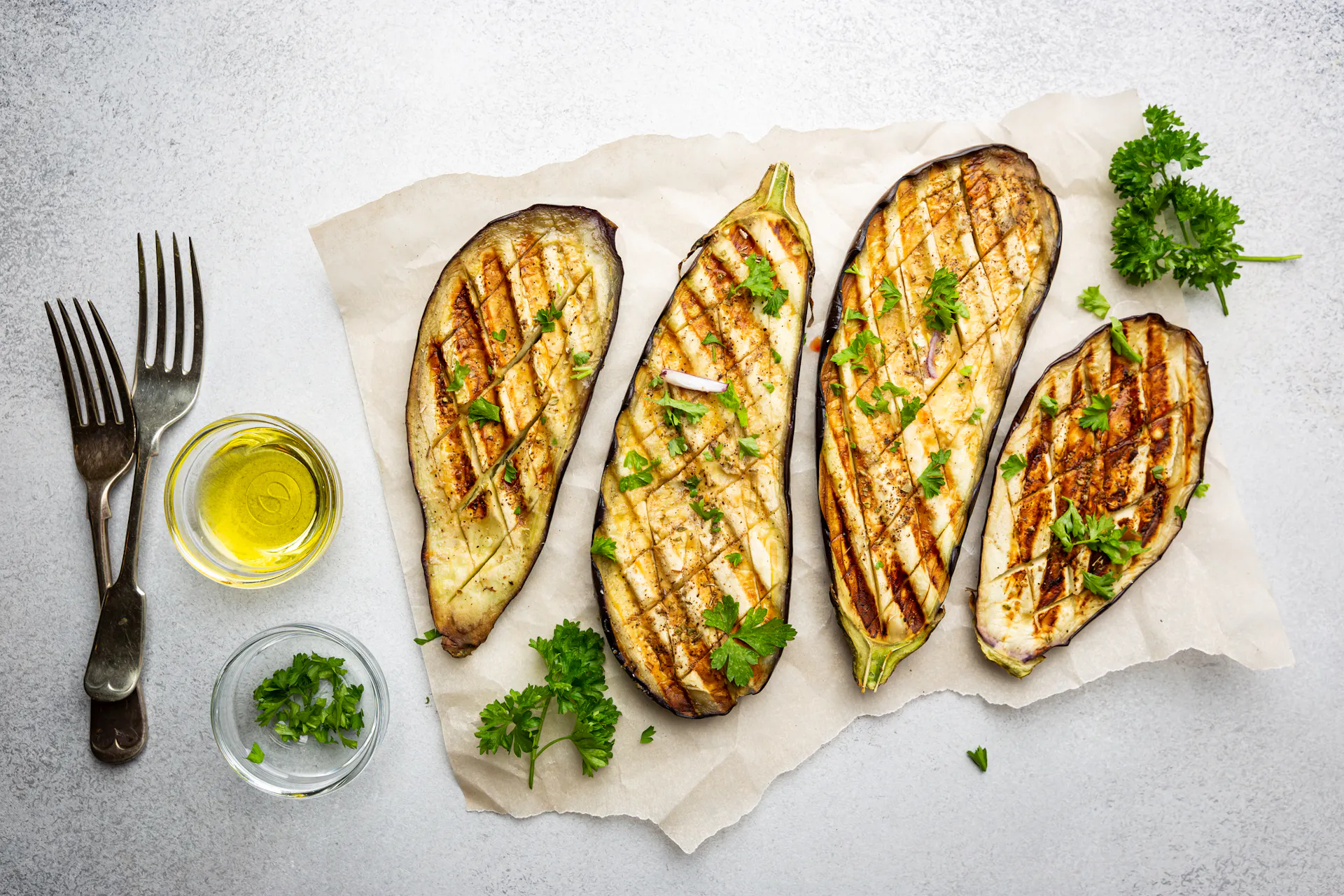 Vier gegrillte Melanzani-Scheiben mit Öl und Petersilie garniert.