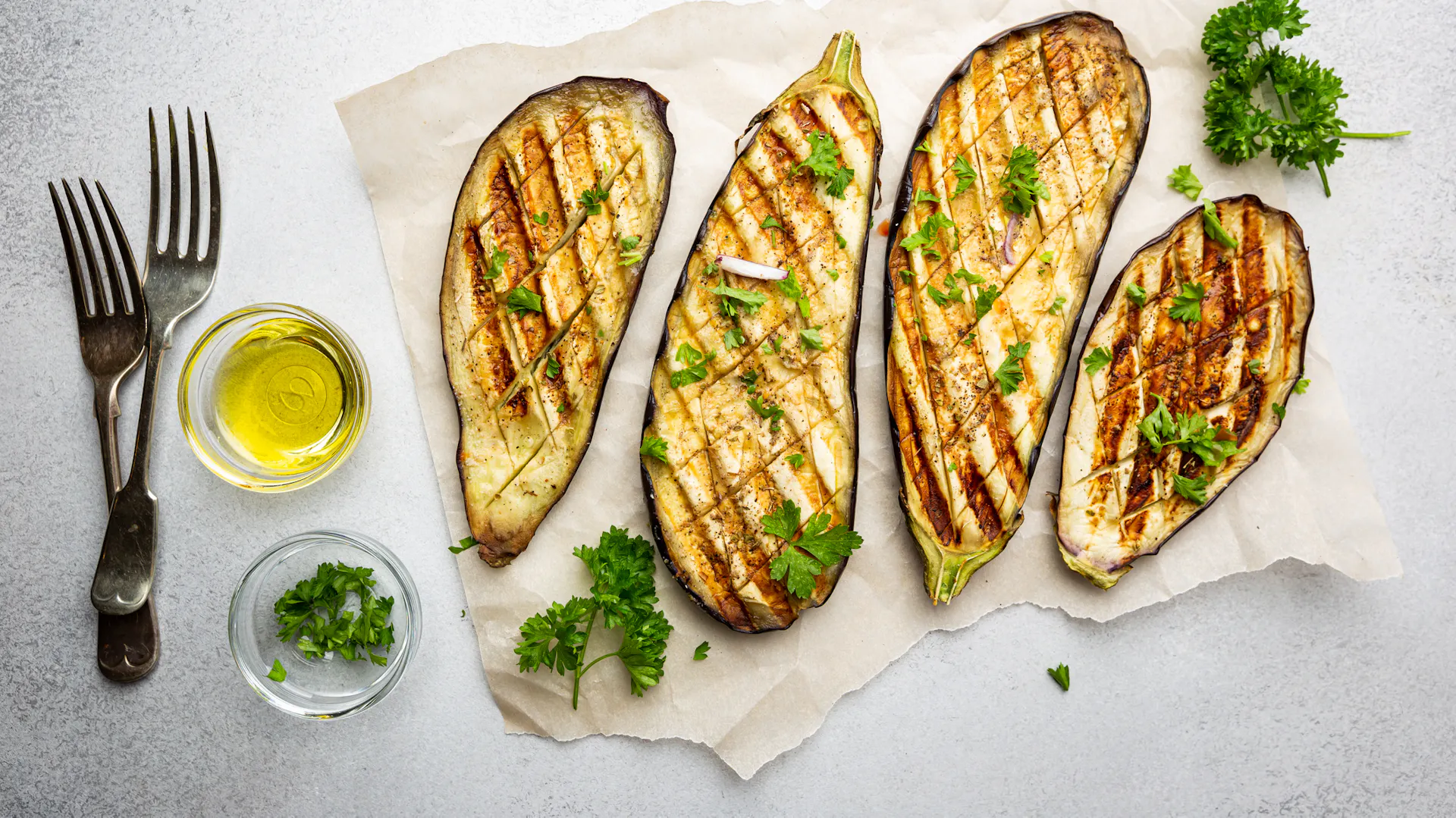 Vier gegrillte Auberginen-Scheiben mit Öl und Petersilie garniert.
