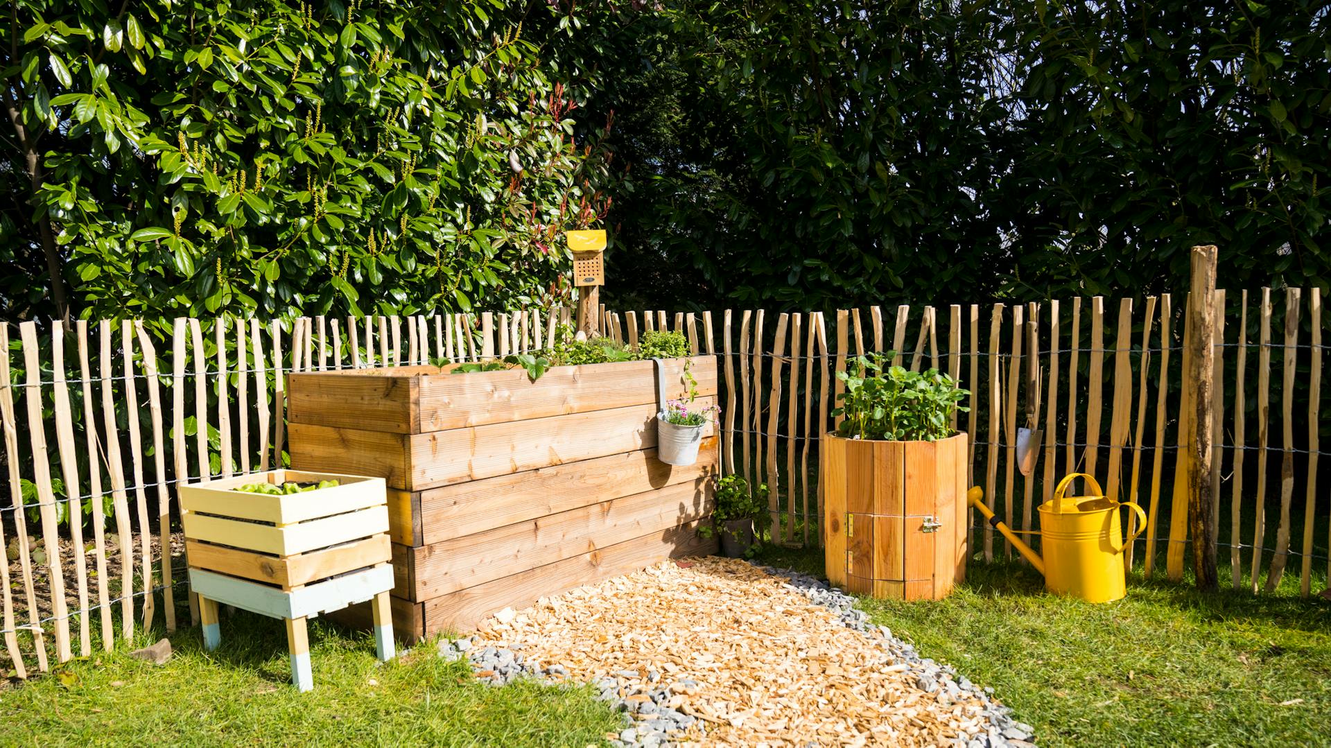 Durch Hochbeete vor Schnecken geschütztes Gemüse neben Kartoffelturm und gelber Gießkanne in Bauerngarten