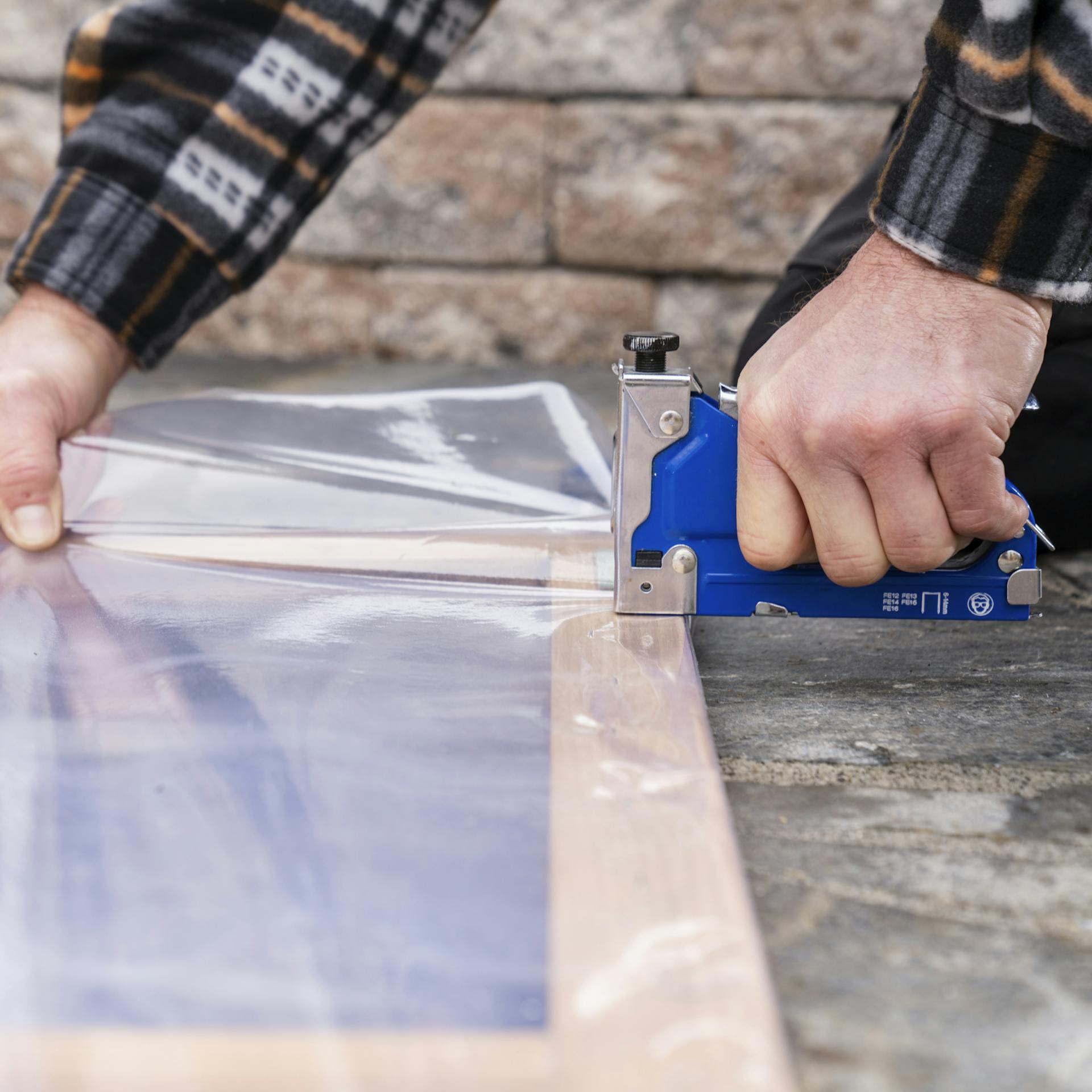 Eine Person bringt mit einem Handtacker Folie auf der Oberseite des Frühbeet-Deckels an.