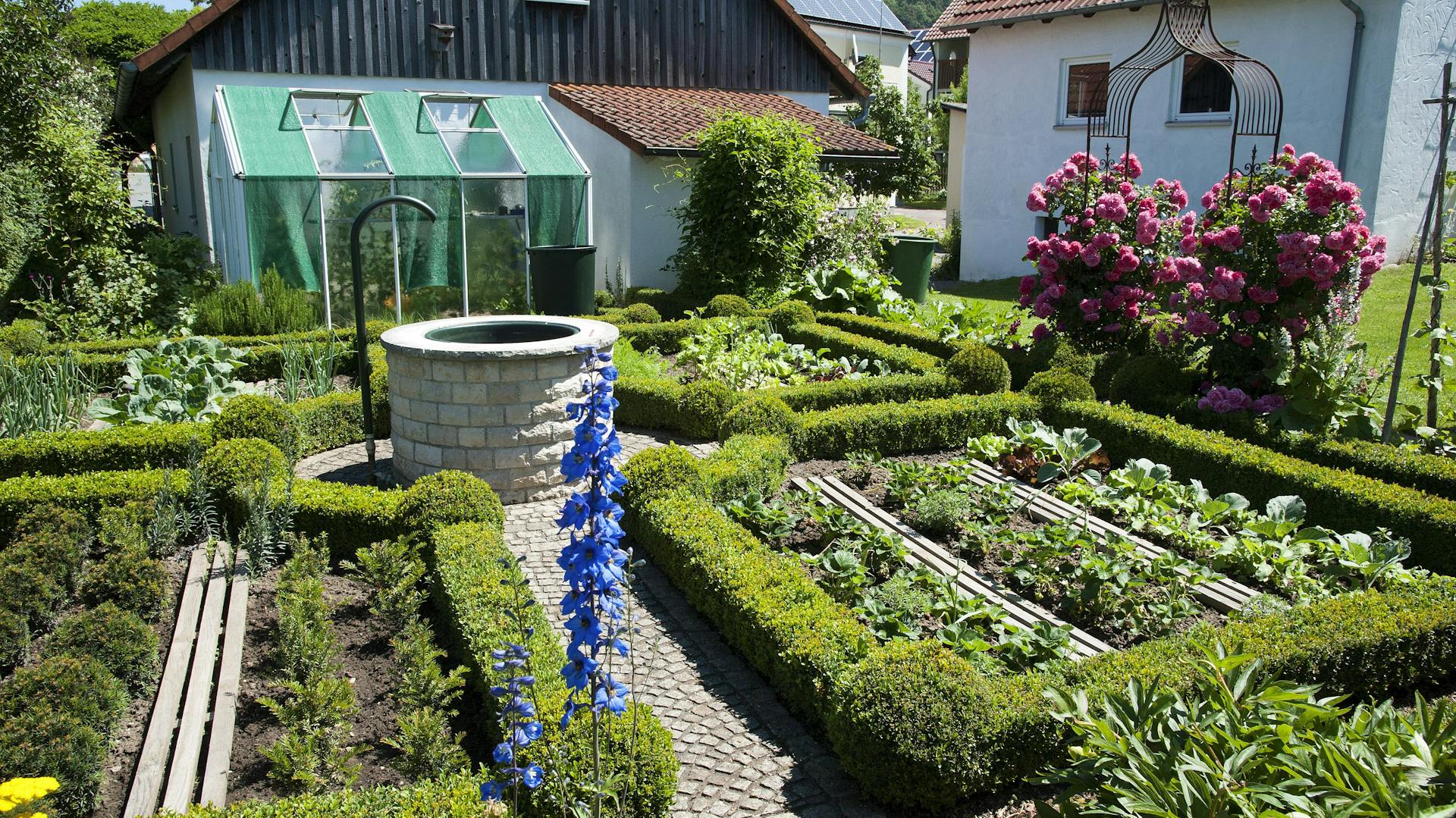 Gemüsegarten gestaltet mit Brunnen, Rankhilfen und Blumen
