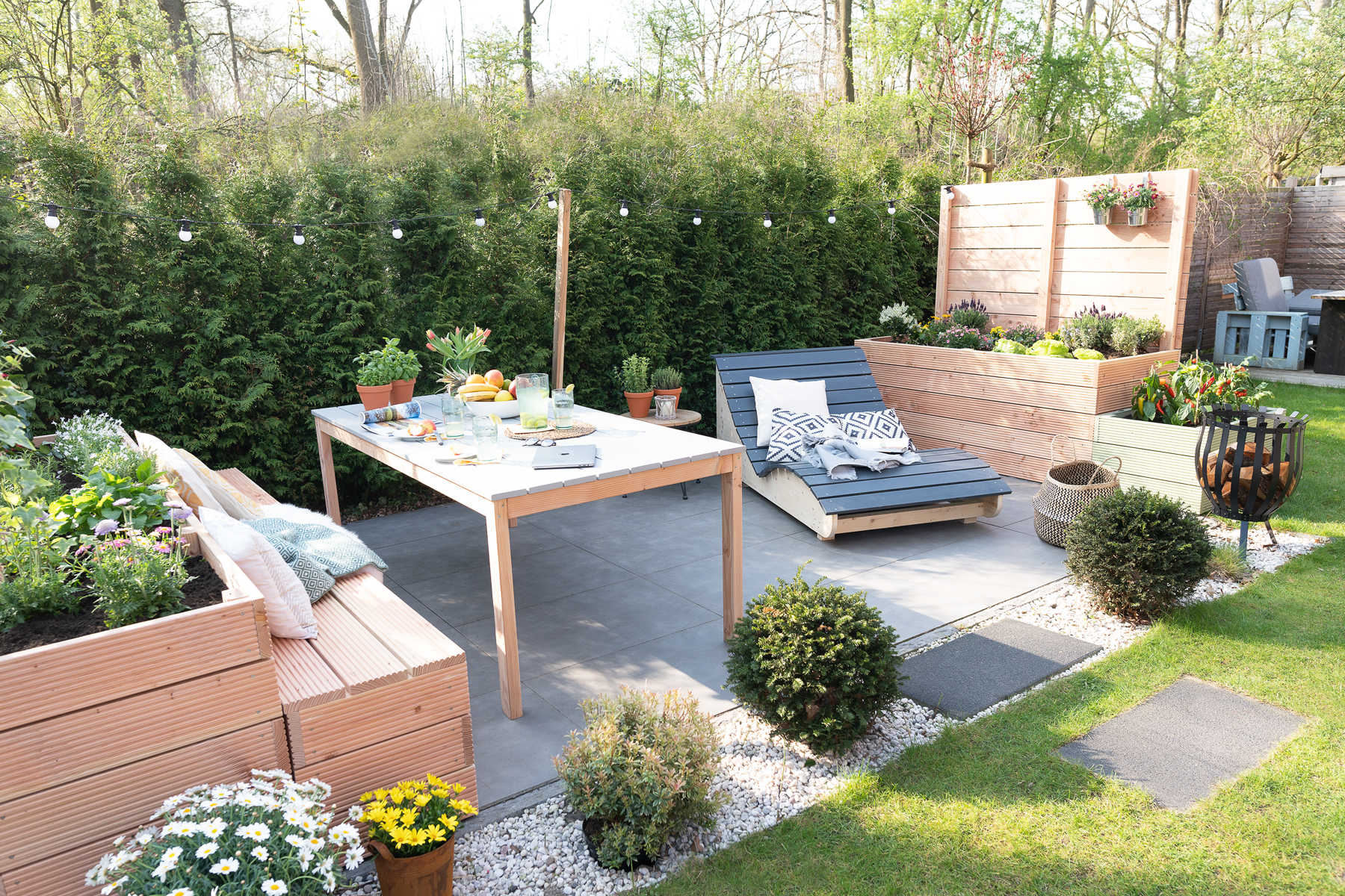 Eine Terrasse, neben der sich an zwei Seiten Hochbeet Alfred mit Sichtschutz und Hochbeet Alfred mit Lichterkette befindet