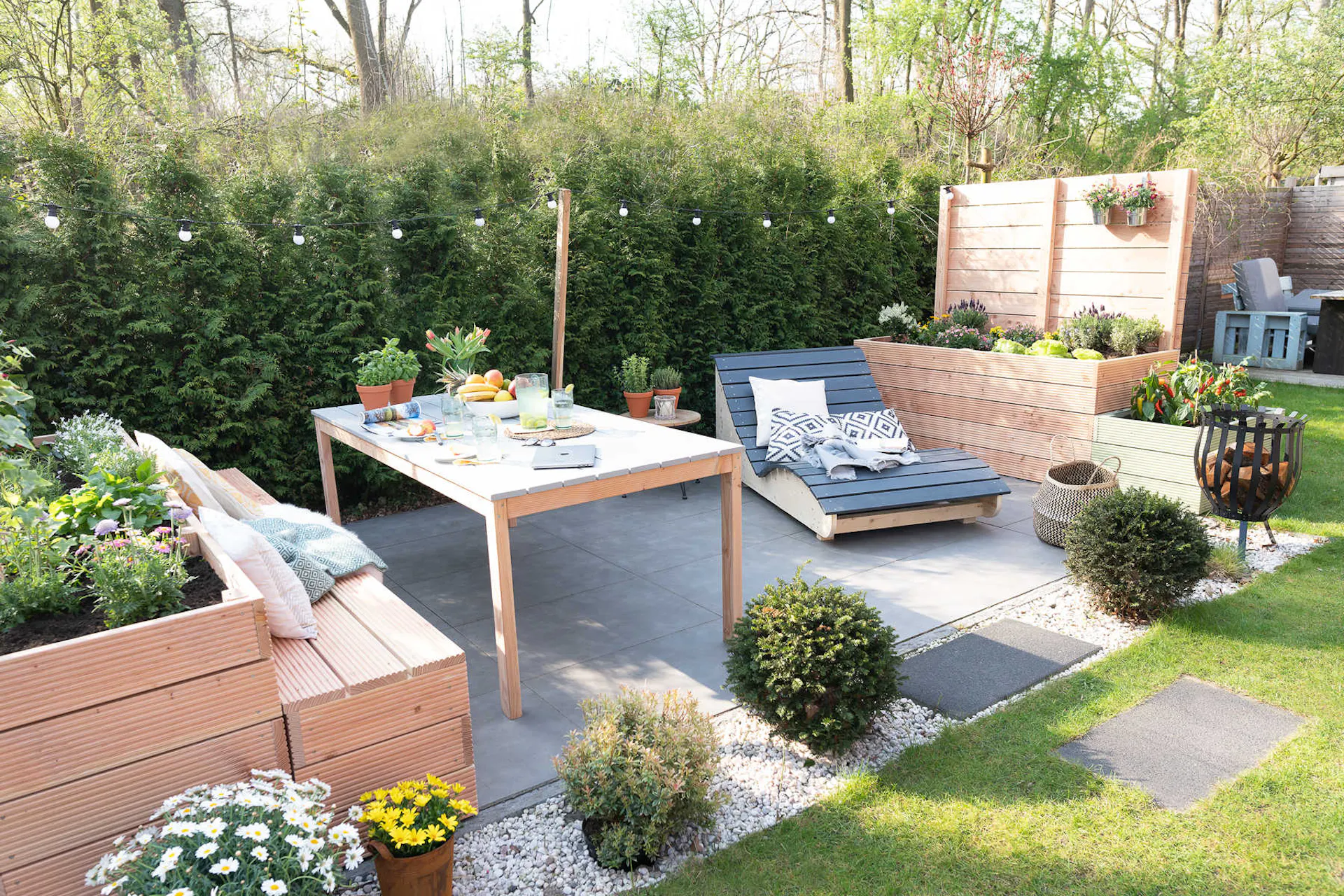 Eine Terrasse, neben der sich an zwei Seiten Hochbeet Alfred mit Sichtschutz und Hochbeet Alfred mit Lichterkette befindet
