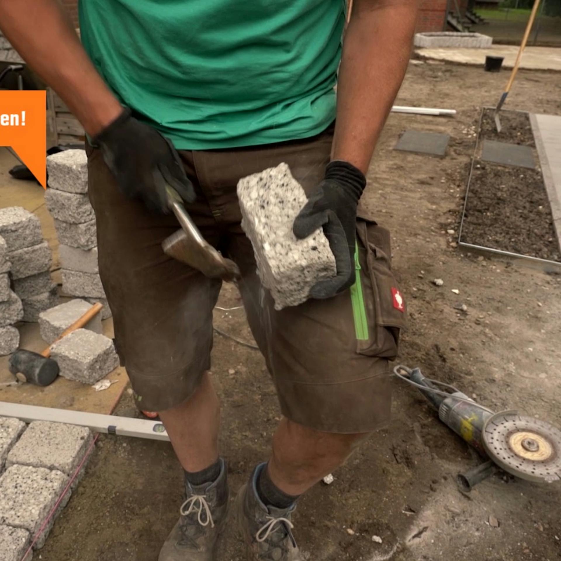 Eine Person bearbeitet einen Stein mit einem Maurerhammer nach