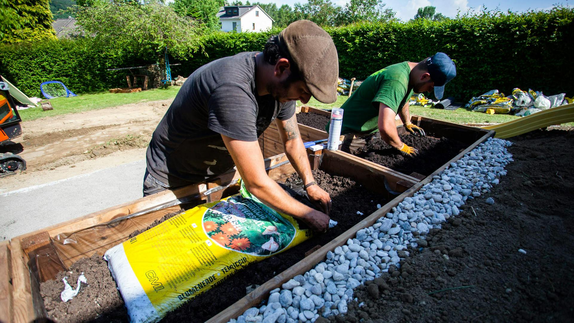 Zwei Heimwerker befüllen ein Hochbeet mit Erde