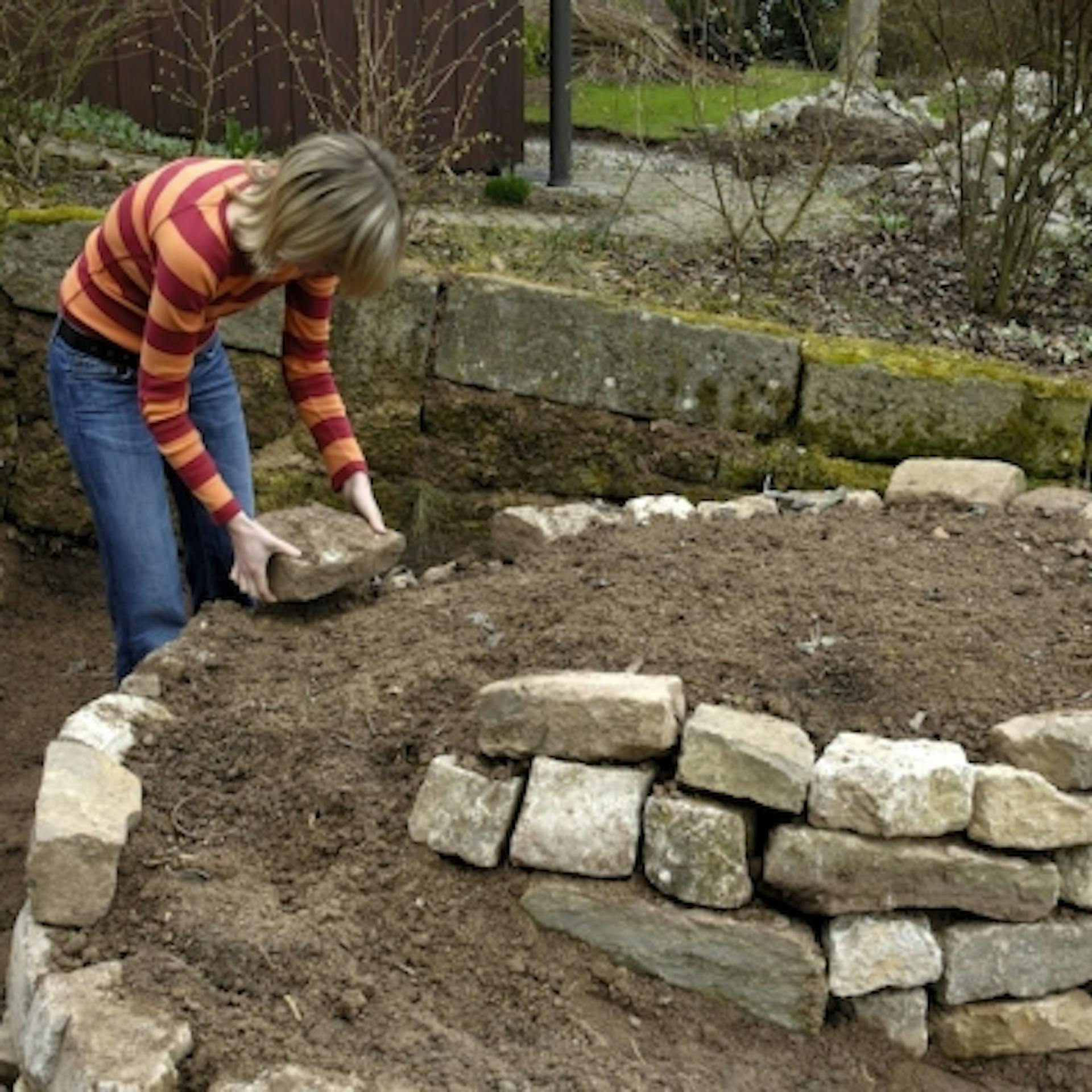 Heimwerkerin legt Kräuterschnecke mit Natursteinen an