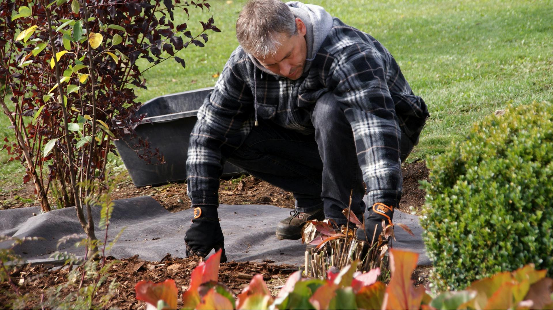 Ein Mann verlegt Unkrautvlies im Garten.
