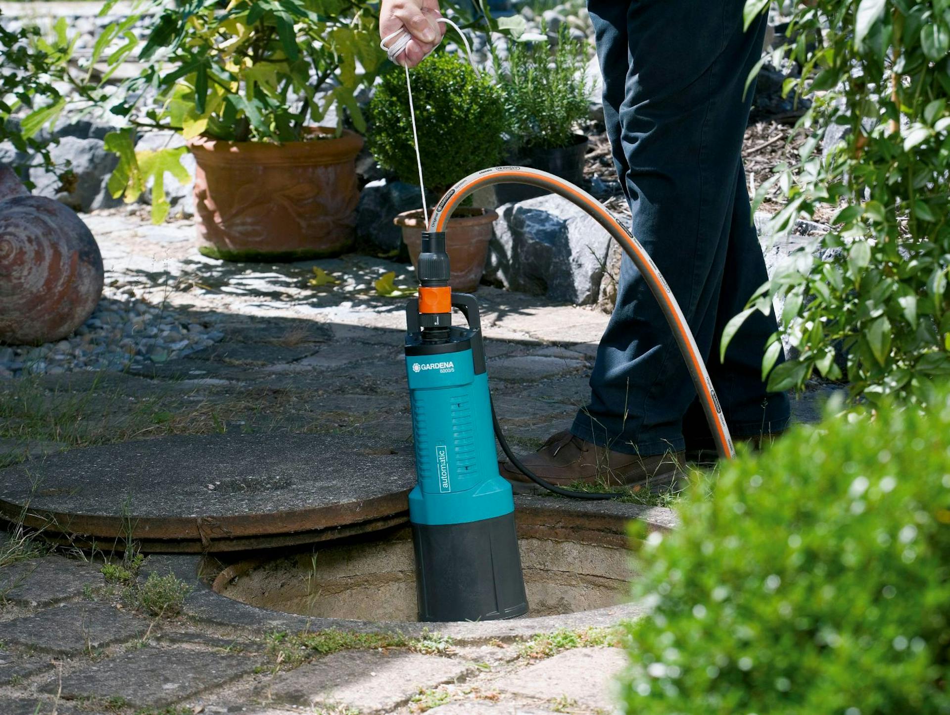 Una mano tiene una pompa a pressione sommersa nel tombino