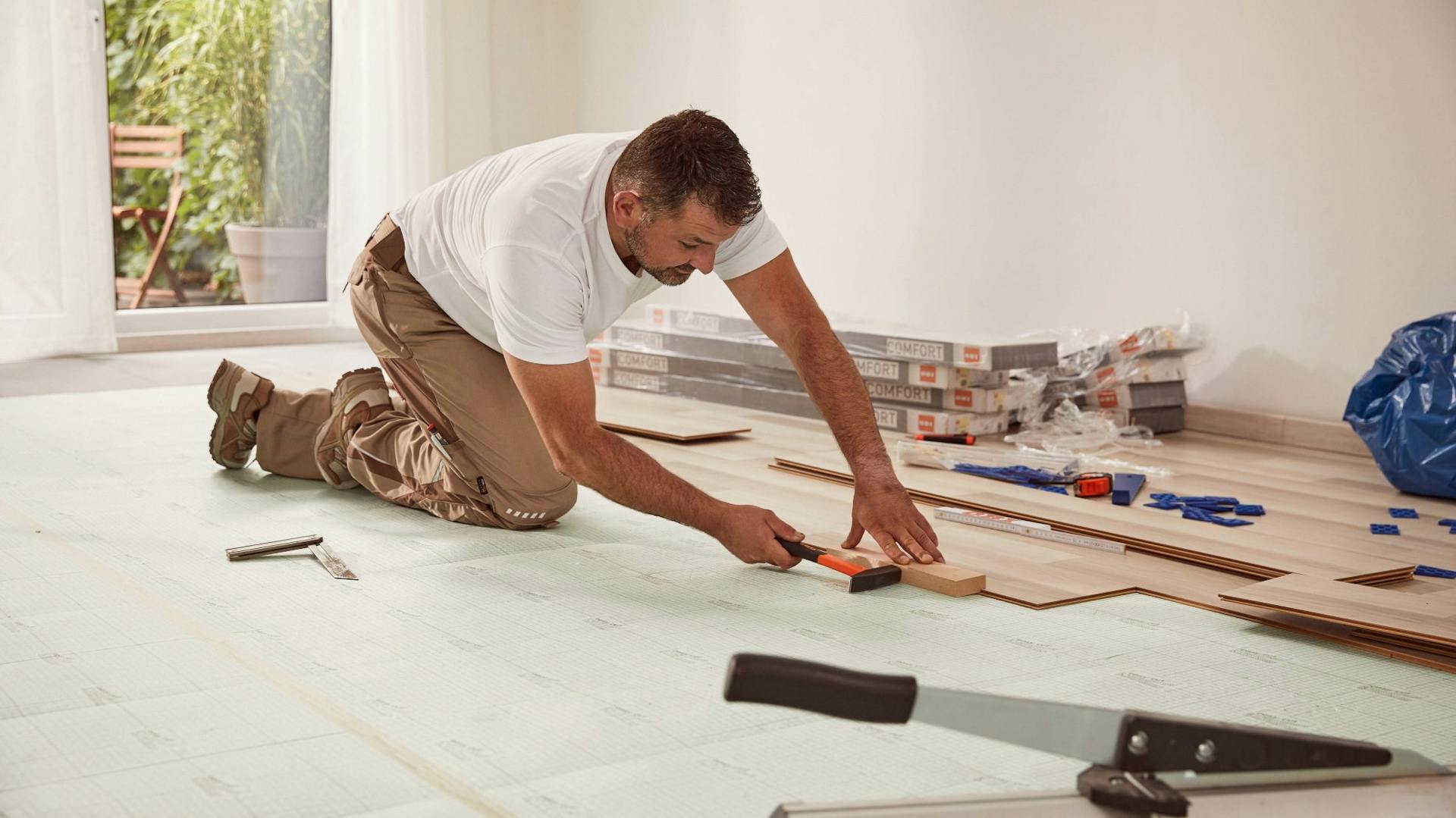 Heimwerker verlegt Laminat mit Hammer und Schlagklotz