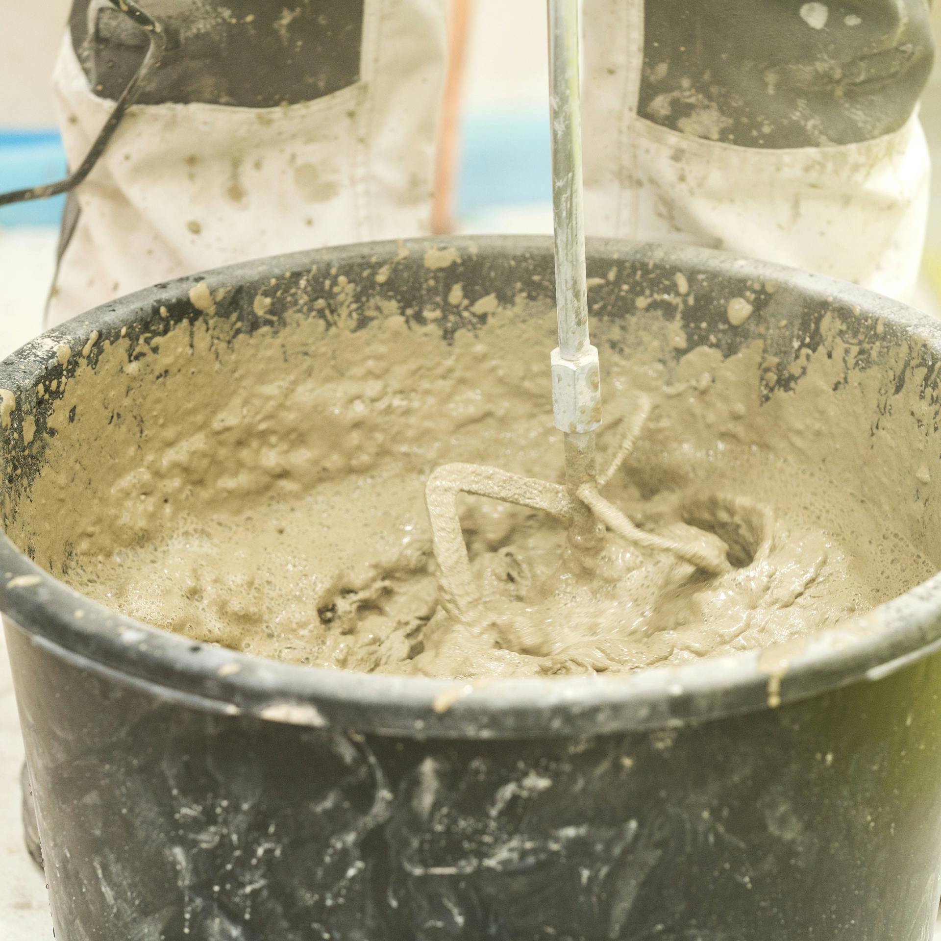 Heimwerker rührt Fliesenkleber mit Bohrmaschine und Quirl an.