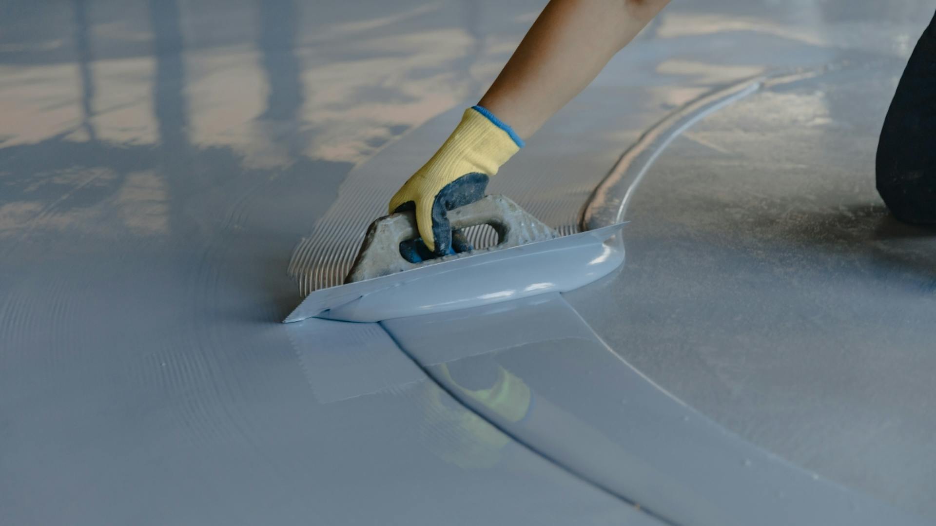 Person verstreicht Epoxidharz mit Spachtel auf Garagenboden