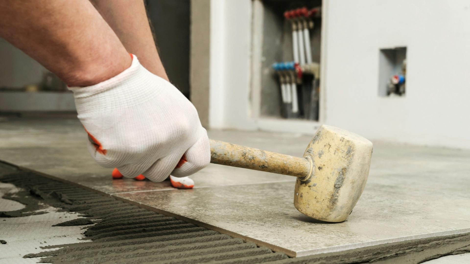 Heimwerker schlägt mit Fliesenhammer auf verlegte Fliese.