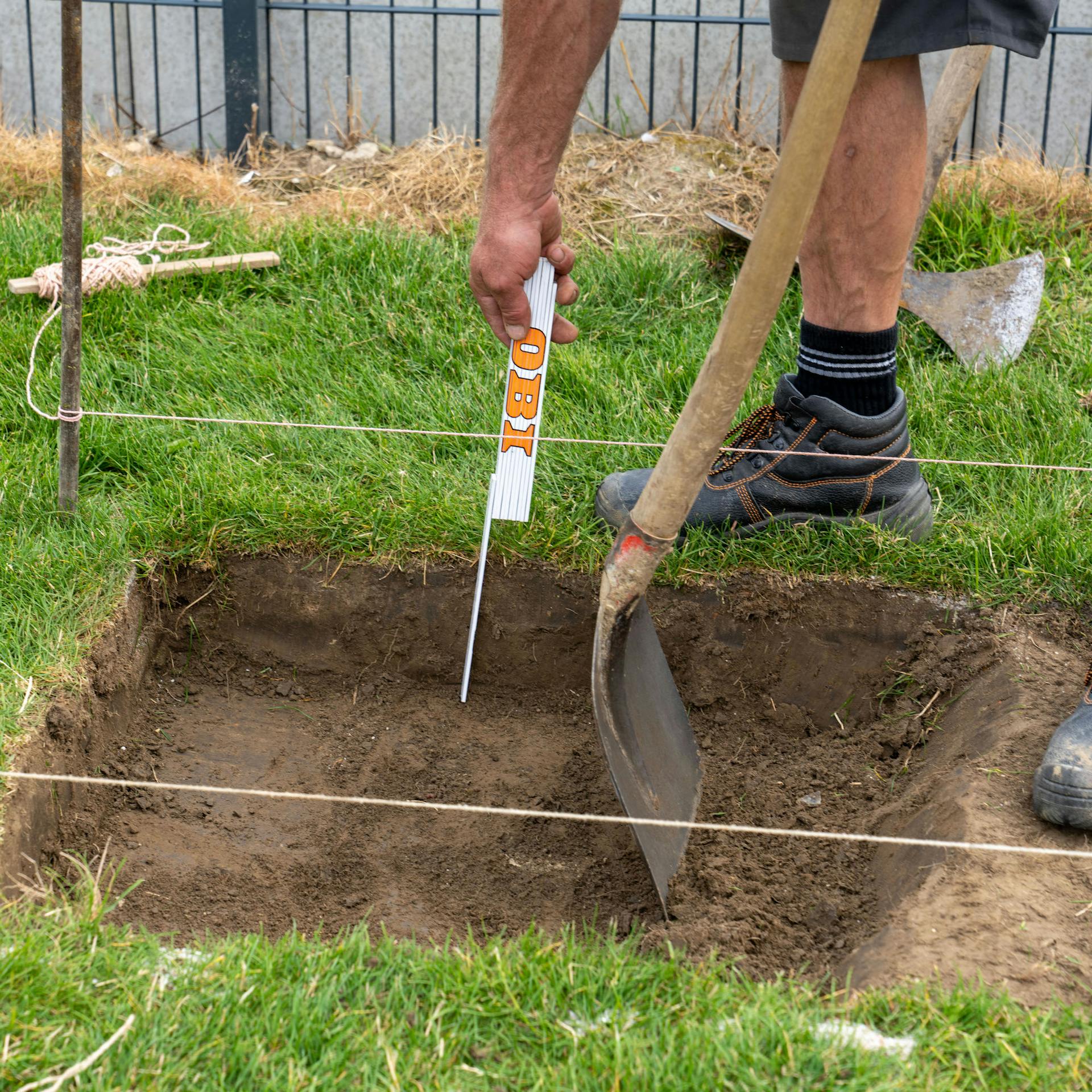 Skladací meter a rýľ vo vykopanej ploche